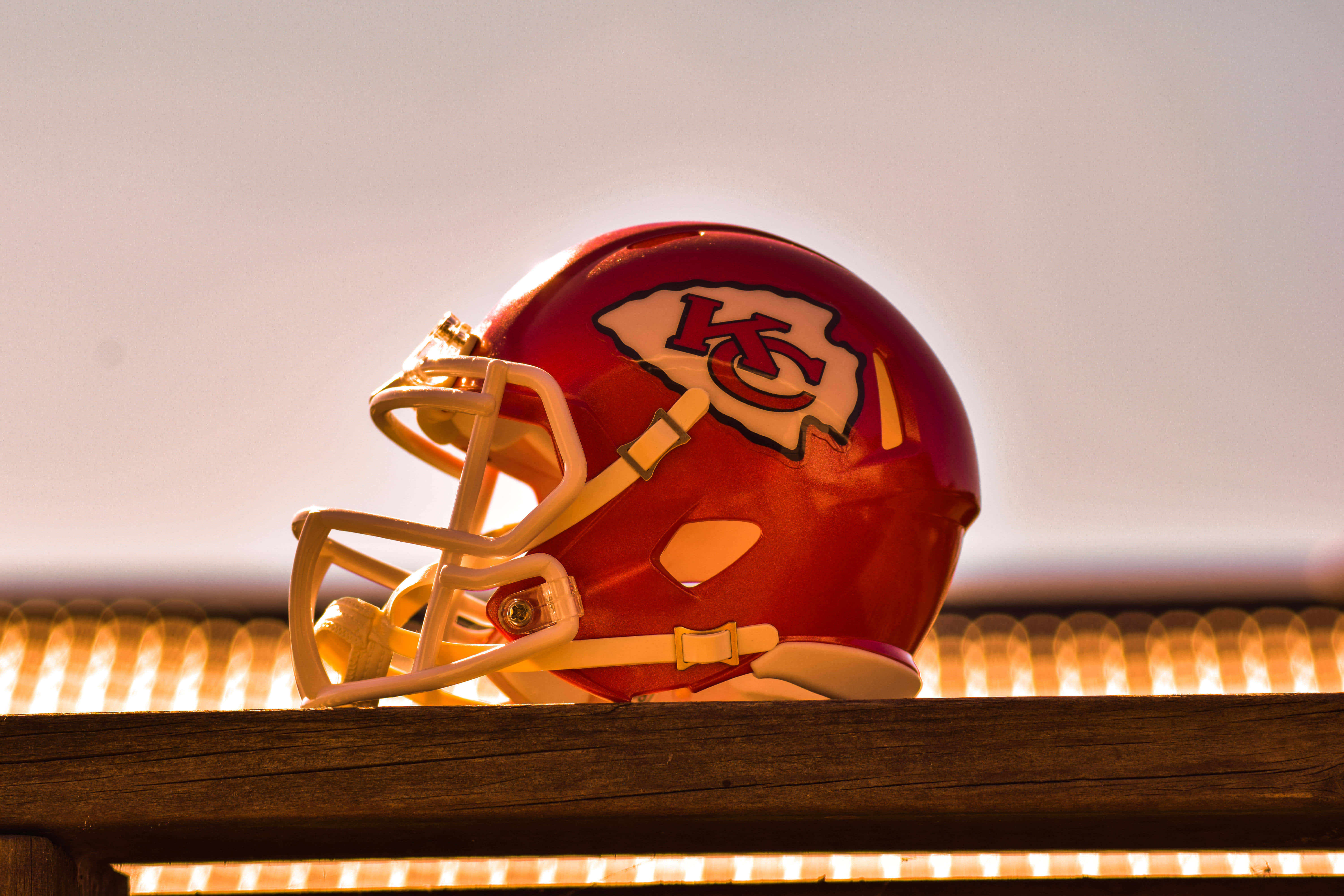 Kansas City Chiefs 4K 桌布 壁紙 — 一個紅色的堪薩斯城酋長隊美式足球頭盔放在一張木長椅上，沐浴在溫暖的金色夕陽光中。