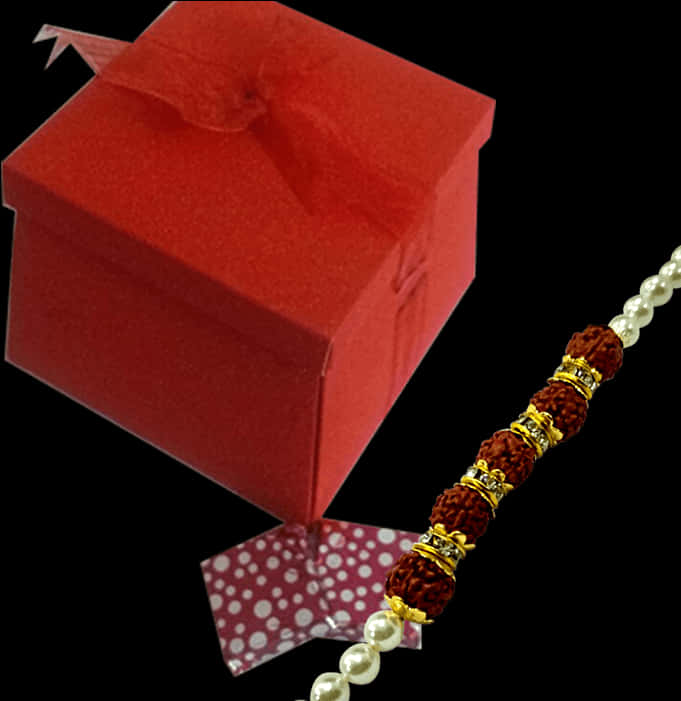Bracelet 桌布 壁紙 — 一個紅色禮物盒附有絲帶，旁邊是傳統的Rakhi手鐲，飾有Rudraksha珠子和珍珠，背景為黑色。
