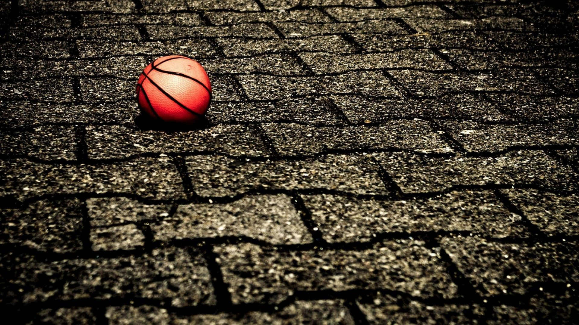 1080p Basketball 桌布 壁紙 — 一個紅色籃球放在裂開的瀝青地上，在戲劇性的低角度燈光下。