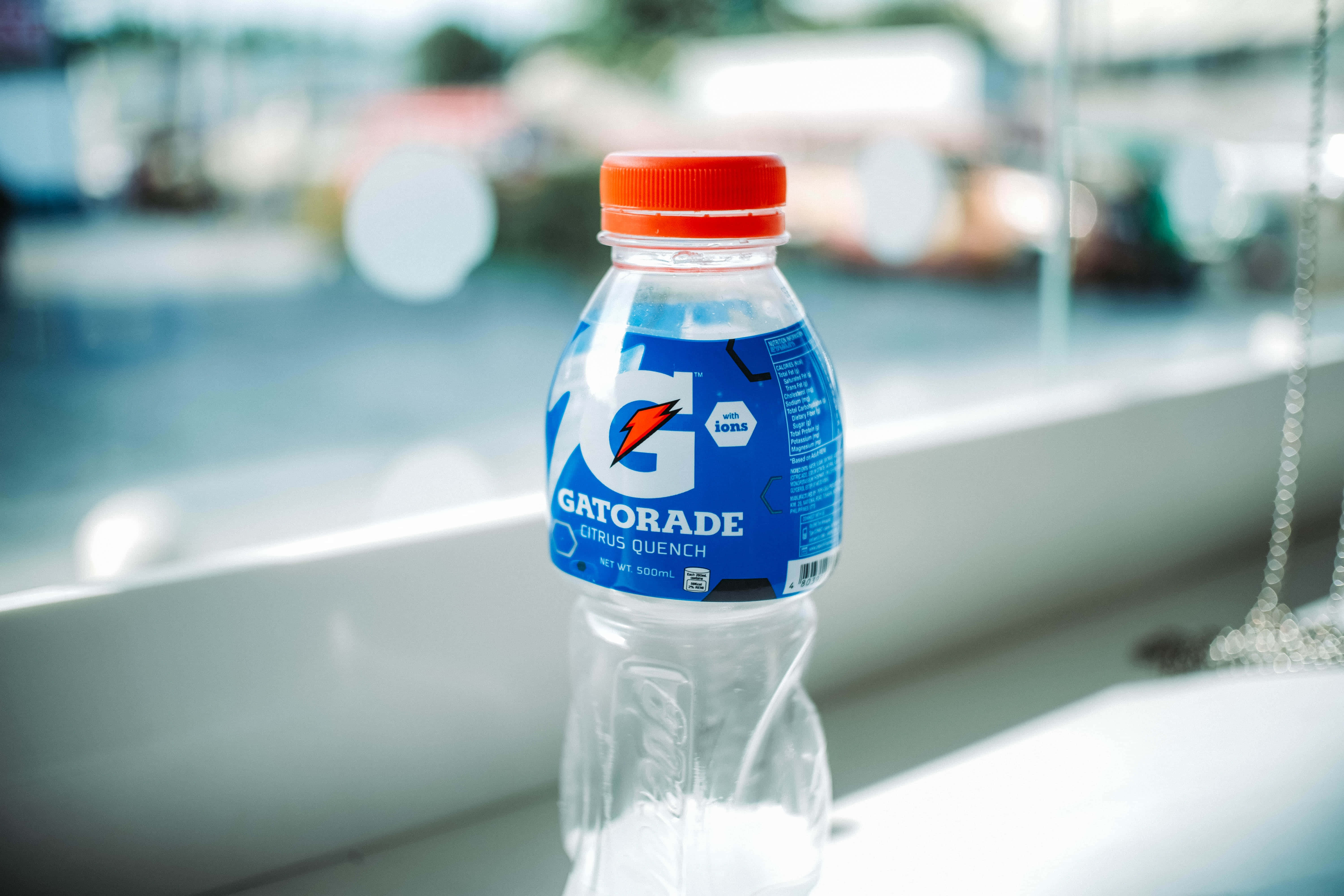 Hydration 桌布 壁紙 — 一個紅色蓋子的透明Gatorade Citrus Quench瓶子放在白色窗台上，背景是模糊的戶外景色。