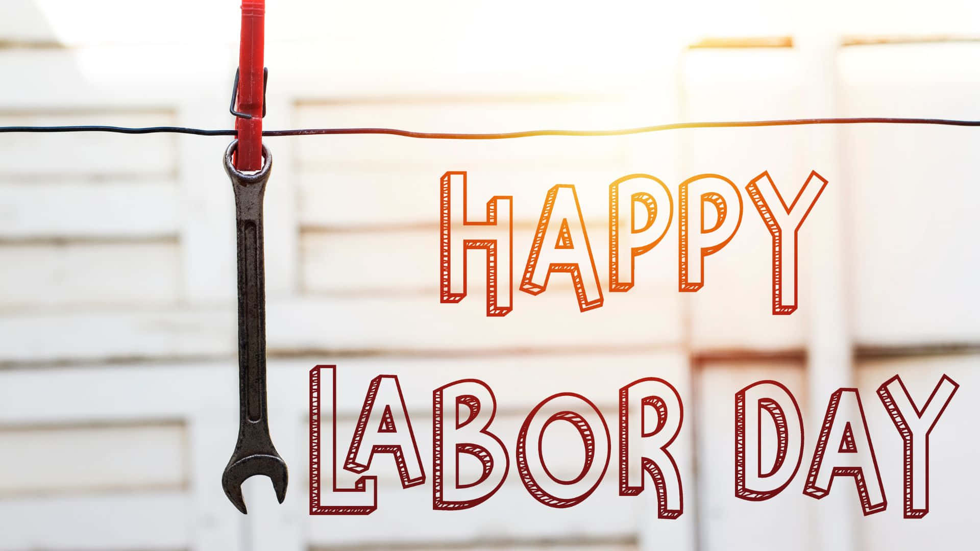 勞動節 桌布 壁紙 — 一個紅色衣夾將扳手夾在繩上，旁邊有「HAPPY LABOR DAY」文字，背景為明亮的白色木質。