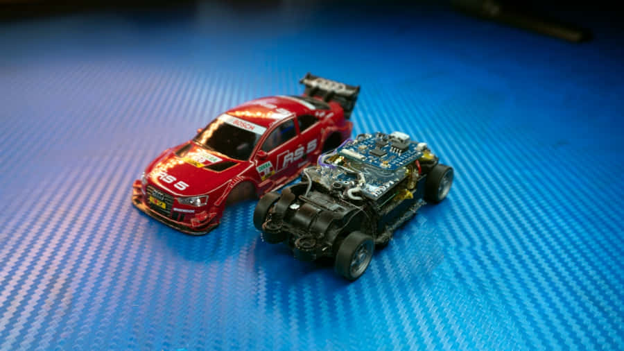 Rc Cars 桌布 壁紙 — 一個紅色賽車模型放在一個透明機器車旁邊，位於藍色碳纖維表面上。