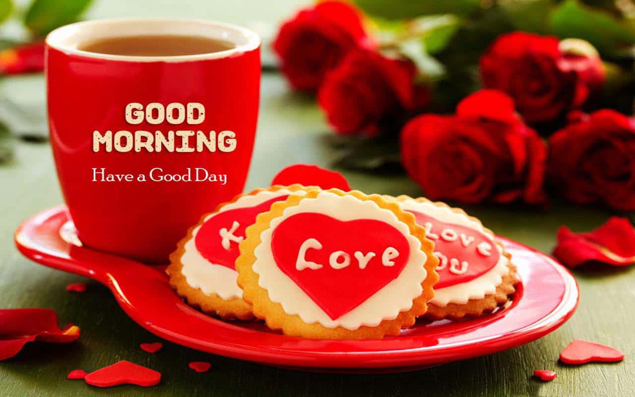  壁紙 — 一個紅色馬克杯上寫著 'GOOD MORNING'，旁邊有心形餅乾和新鮮紅玫瑰，放在綠色木桌上。