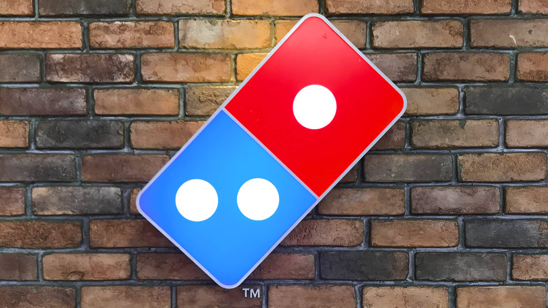 Dominos Pizza 桌布 壁紙 — 一個紅藍色的 Domino's pizza 標誌牌靠在風化的磚牆上。