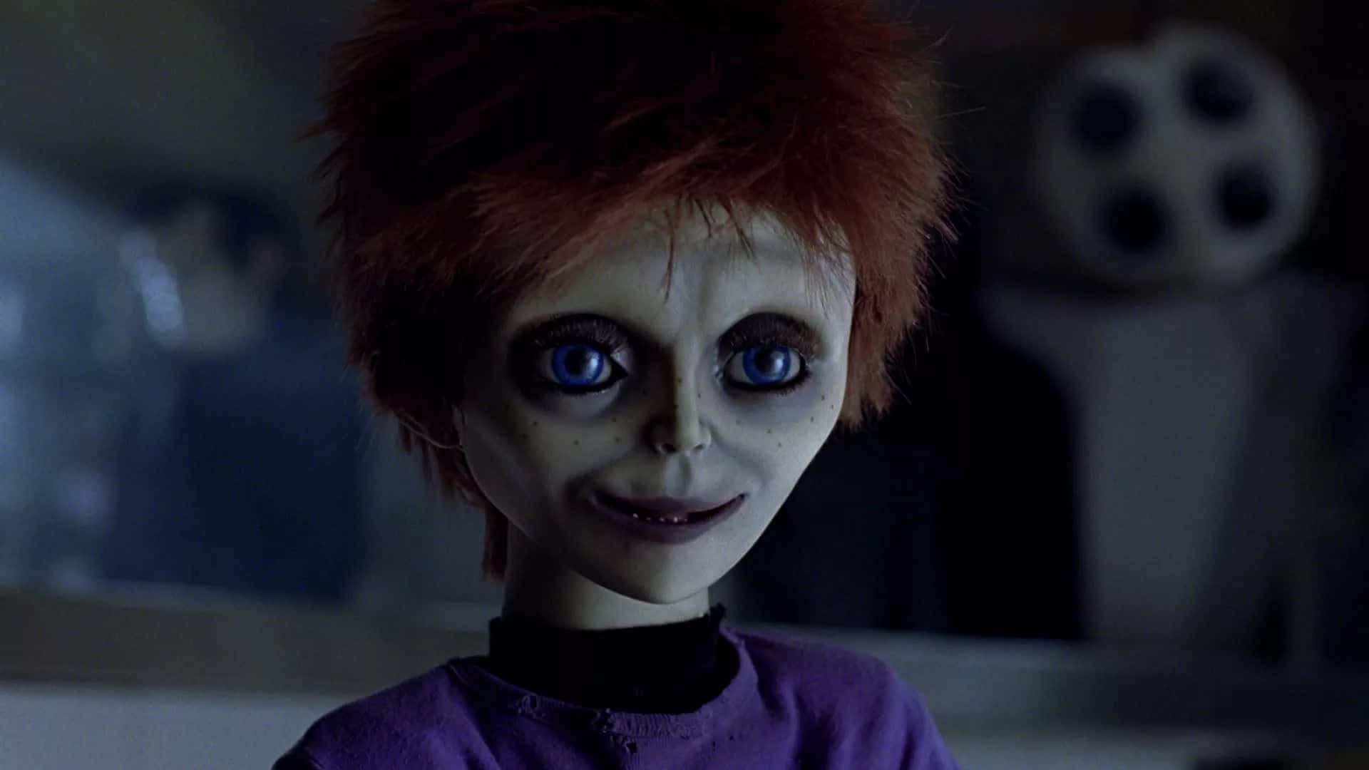 Chucky Doll 桌布 壁紙 — 一個紅髮、藍色發光眼睛的恐怖娃娃，在昏暗的房間裡，背景有膠卷，凝視著前方。