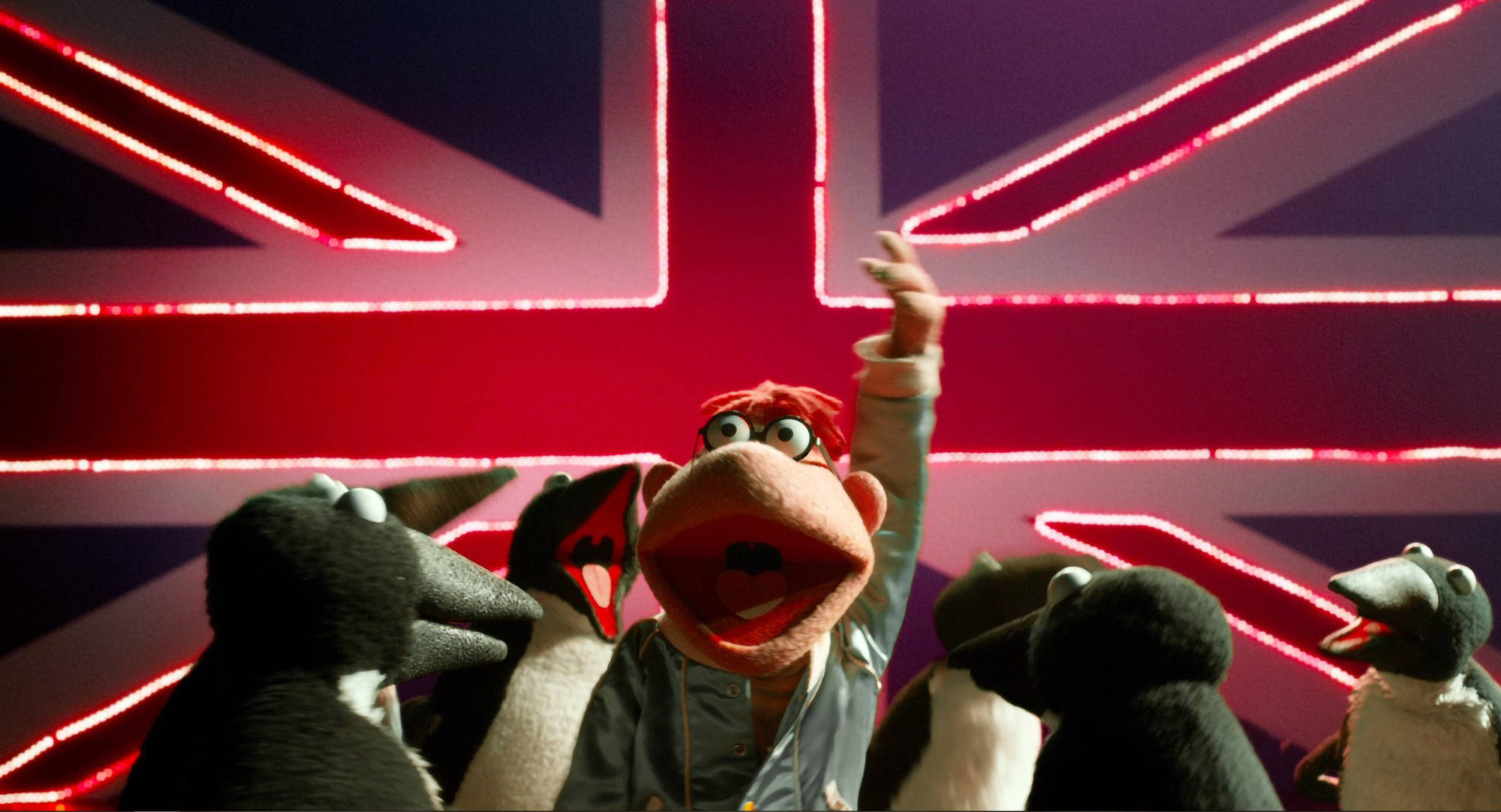 muppets 桌布 壁紙 — 一個紅髮布偶與企鵝在發光的霓虹英國國旗前歡呼。