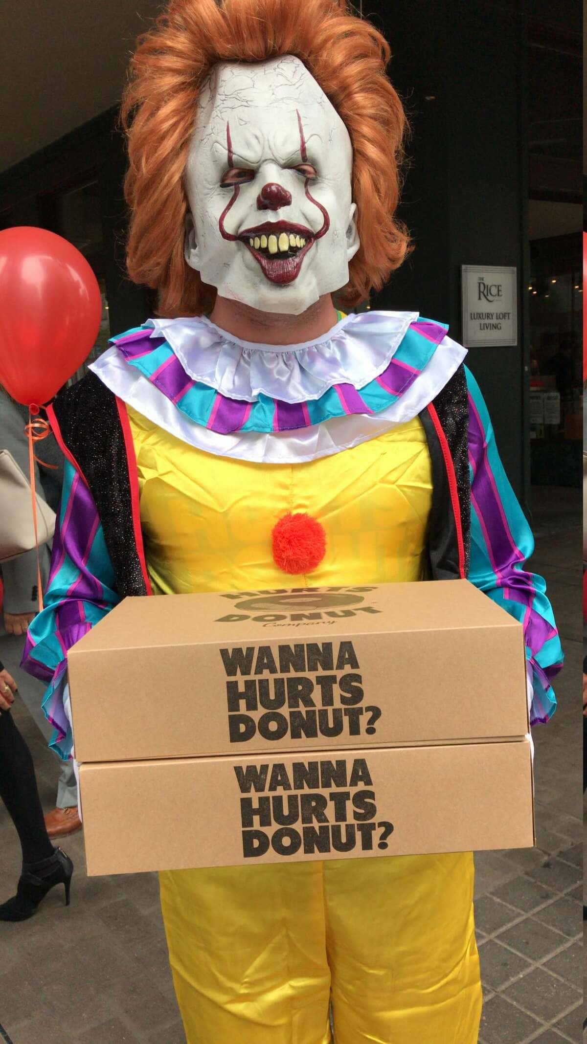 恐怖動圖 桌布 壁紙 — 一個紅髮白臉的恐怖小丑手持兩個寫著「WANNA HURTS DONUT?」的盒子，旁邊有一個紅色氣球漂浮著。