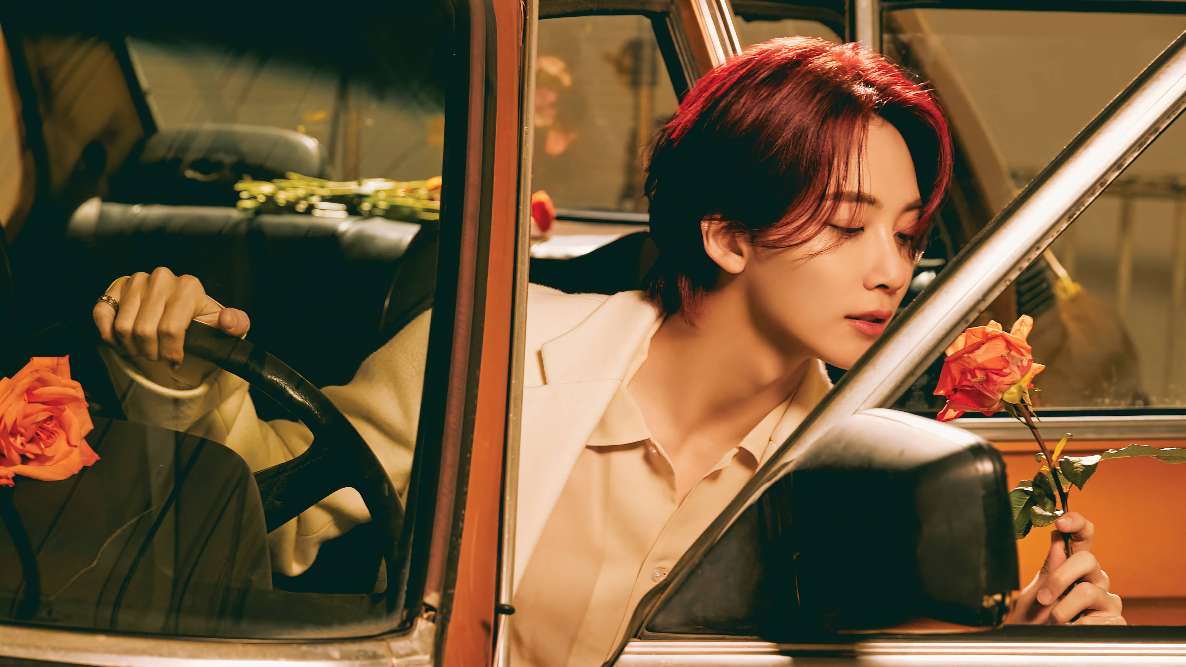 yoon jeonghan 桌布 壁紙 — 一個紅髮的人坐在一輛復古車裡，手持一朵玫瑰，沐浴在溫暖的金色光線中。