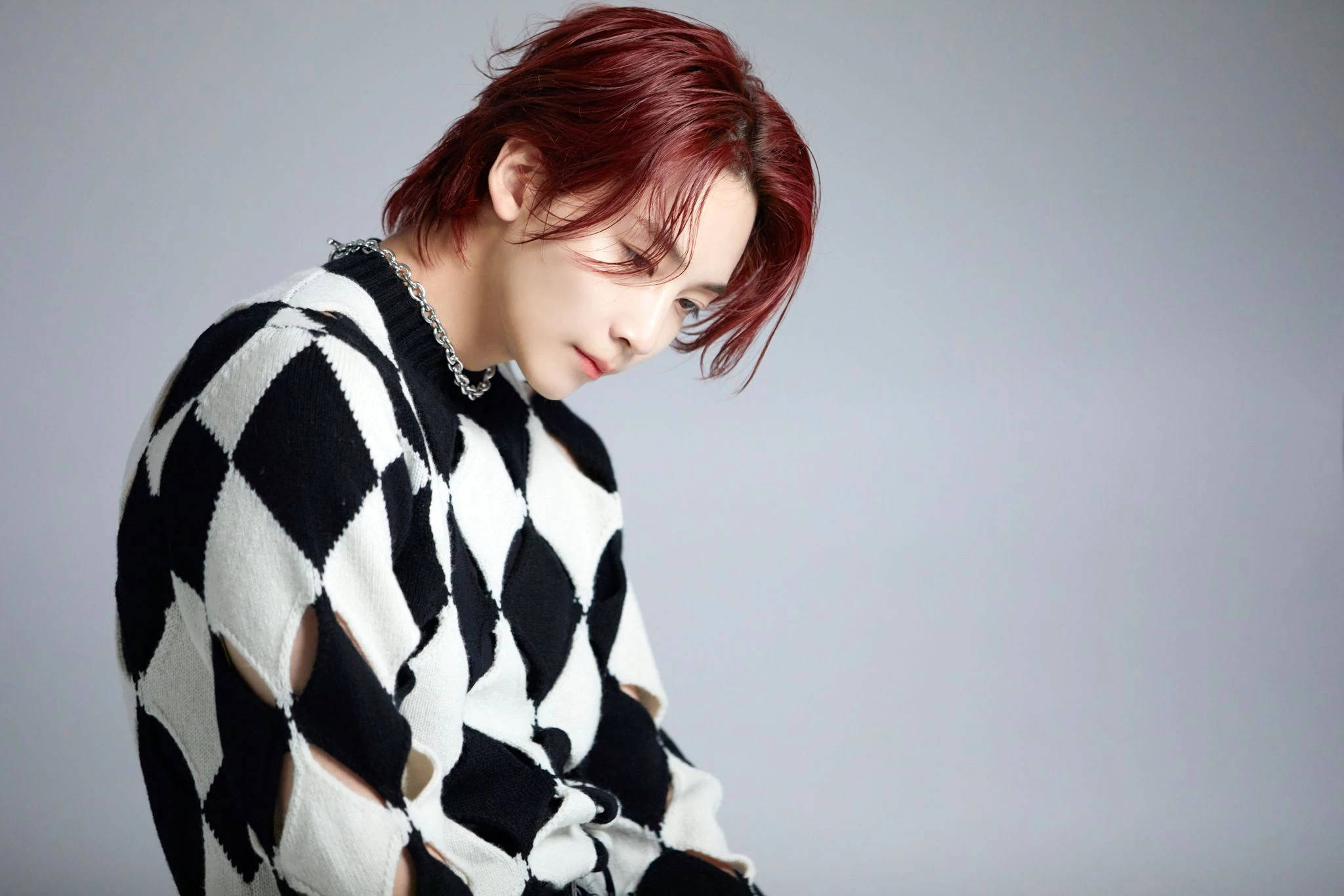 yoon jeonghan 桌布 壁紙 — 一個紅髮的人穿著黑白菱形圖案毛衣，背景是純灰色。