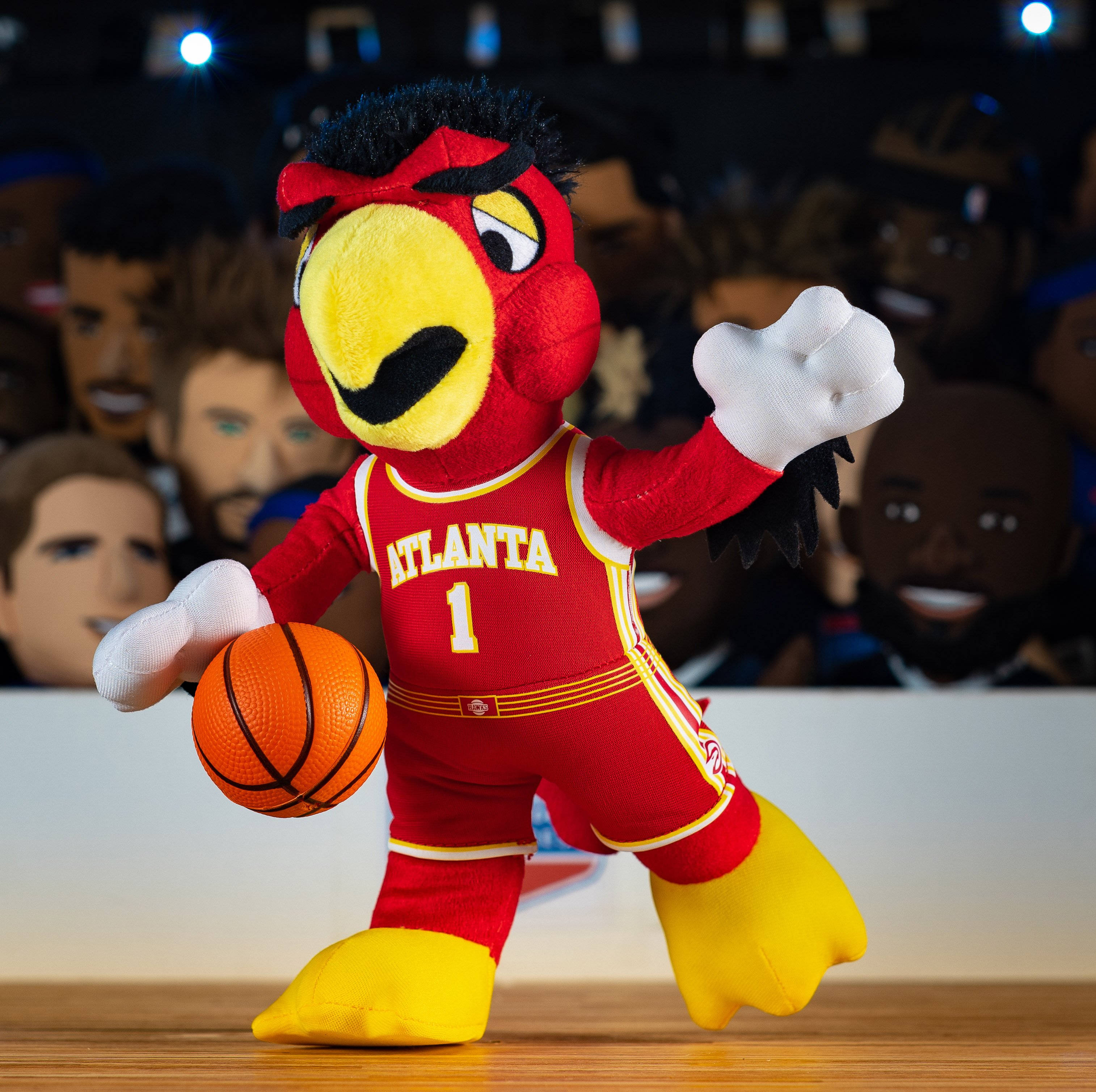 Hawks 桌布 壁紙 — 一個紅黃色的亞特蘭大老鷹隊吉祥物絨毛娃娃在木地板上運球，背景是模糊的人群頭部。