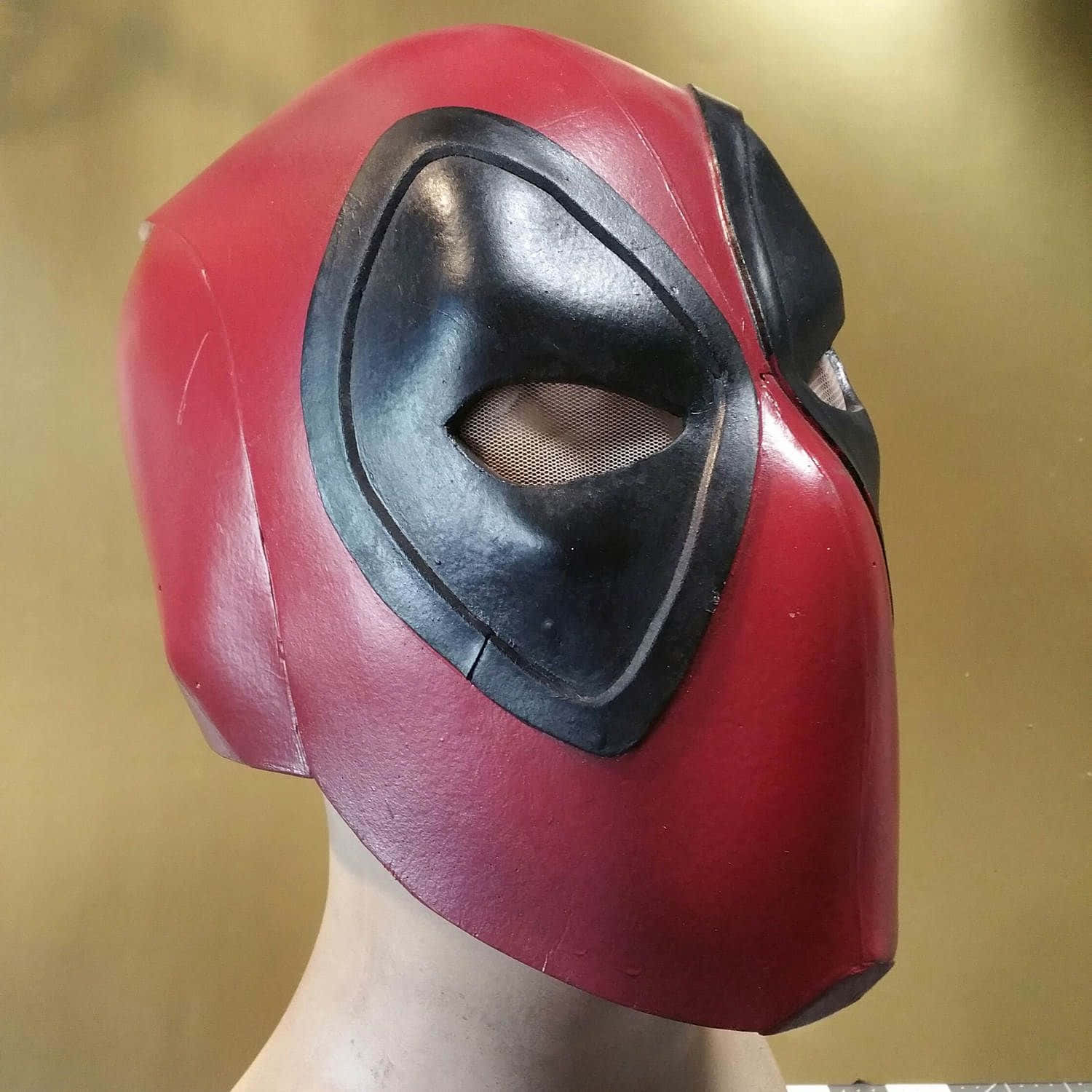 Deadpool Mask 桌布 壁紙 — 一個紅黑色的死侍面具展示在人體模型頭上，背景是溫暖的金色。