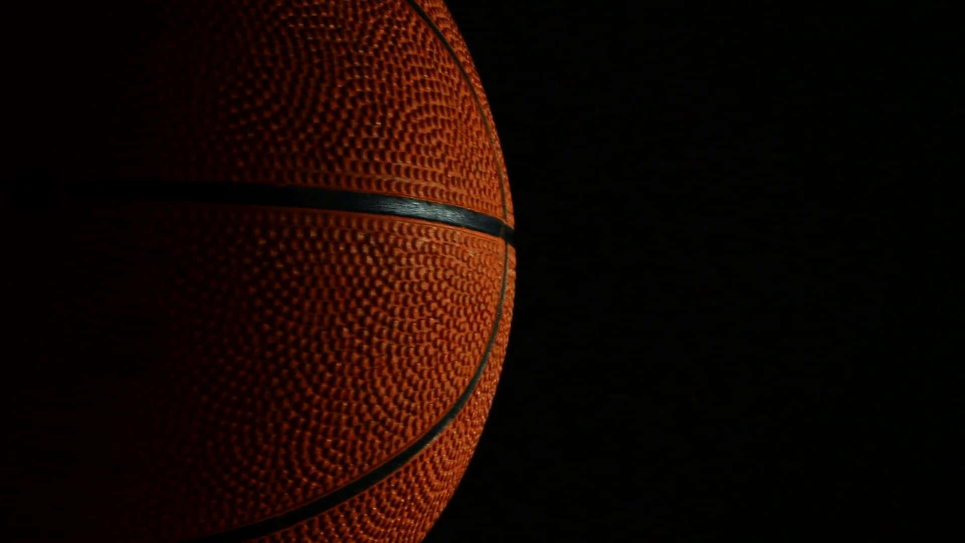 1080p Basketball 桌布 壁紙 — 一個紋理橙色的籃球在純黑色背景下被照亮的特寫。