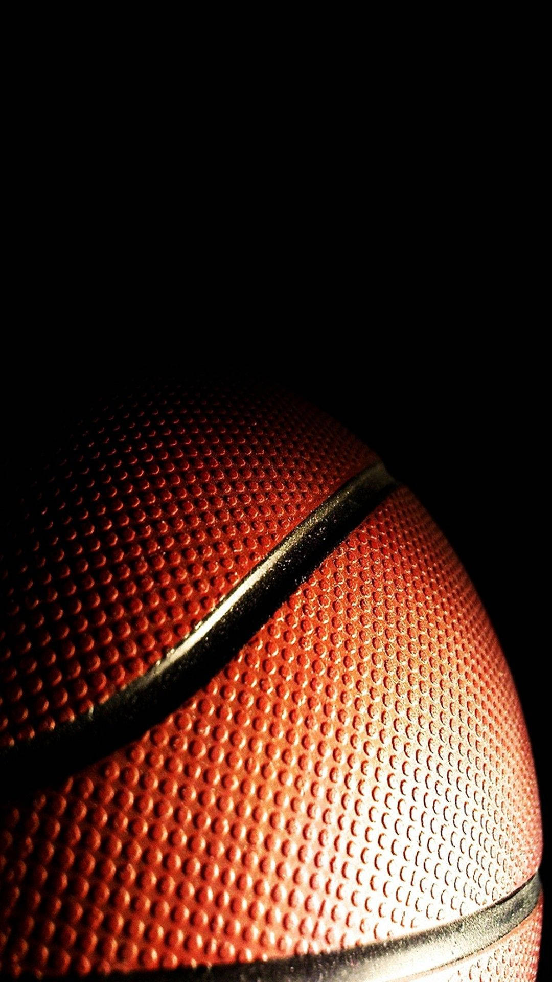 NBA iPhone 桌布 壁紙 — 一個紋理橙色籃球的特寫，在黑色背景下被戲劇性的燈光照亮。
