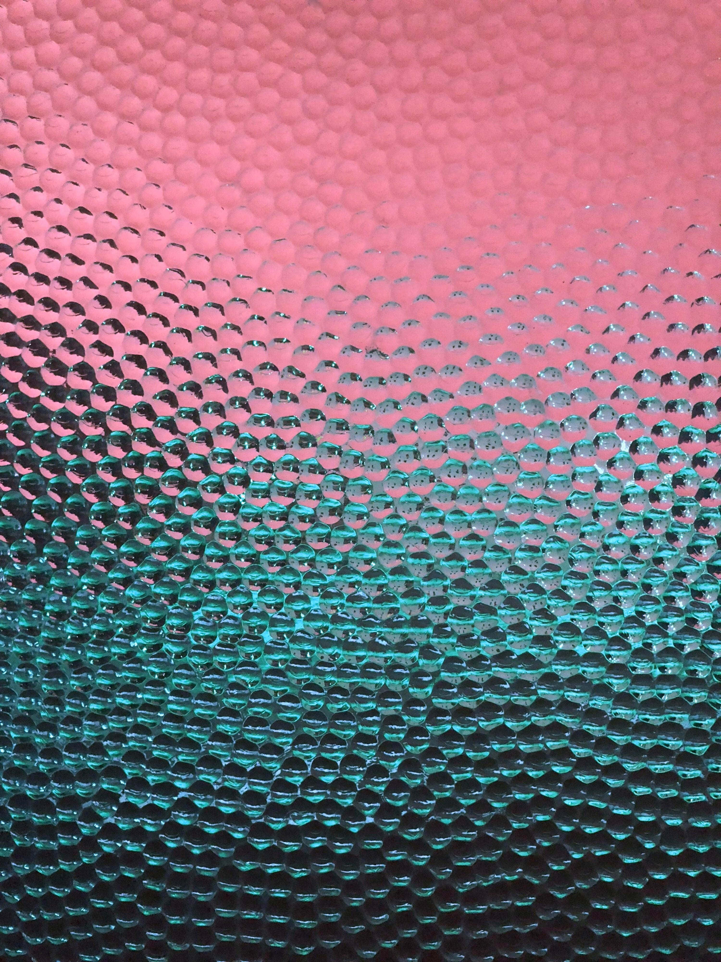 桌布 壁紙 — 一個紋理表面的特寫，帶有從粉紅色到藍綠色的漸變，呈現重複的氣泡狀圖案。