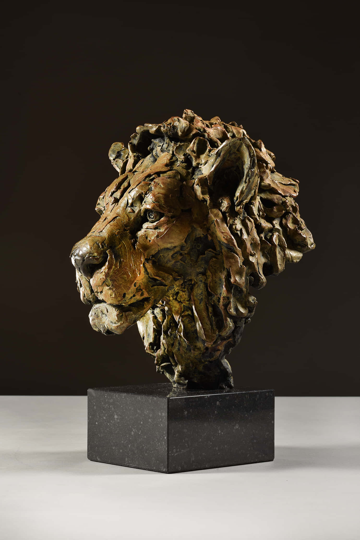 Lion Head 桌布 壁紙 — 一個紋理豐富的青銅獅頭雕塑，帶有狂野的鬃毛，放置在黑色大理石底座上，背景為深色。