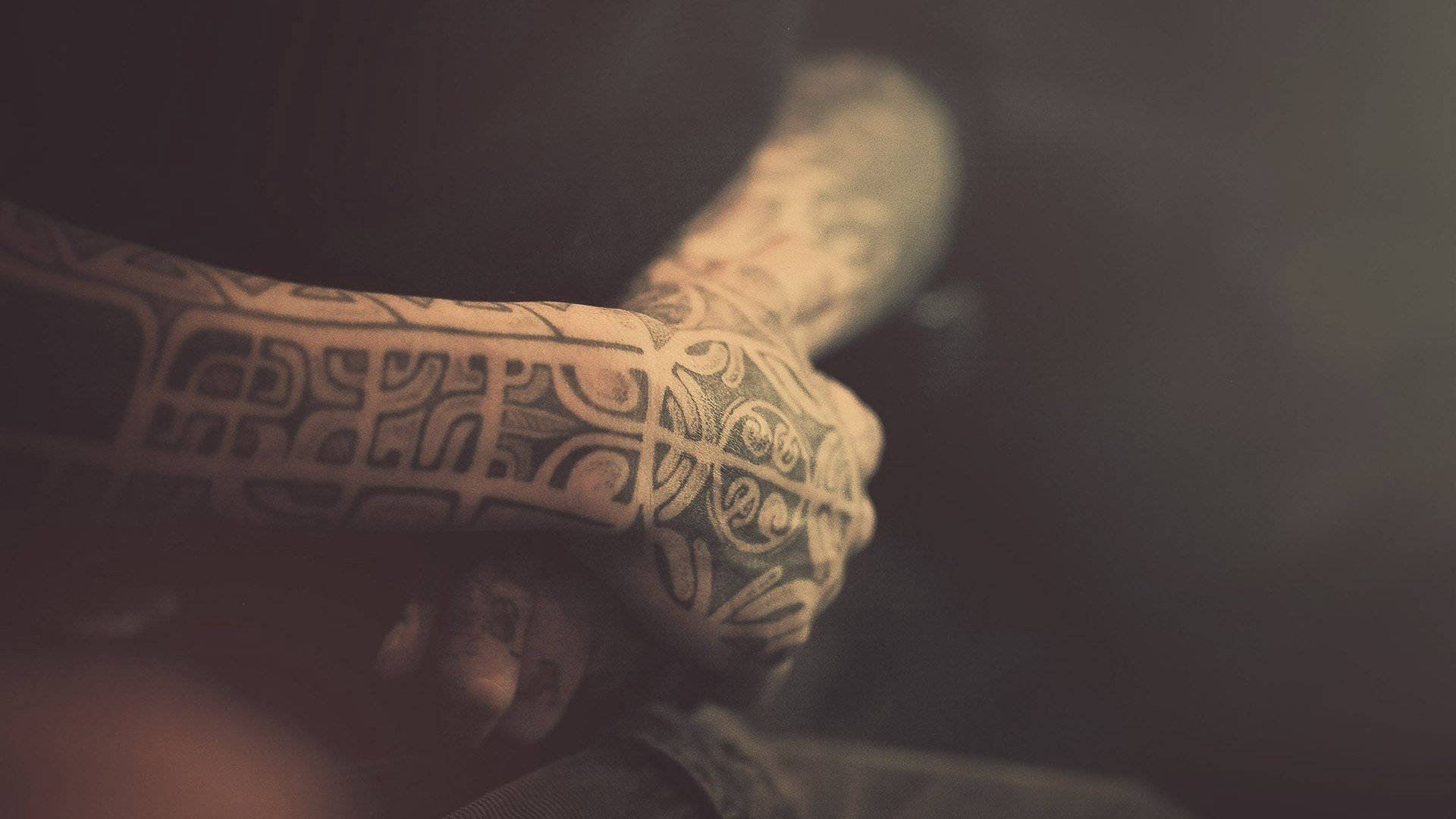 Tattoo 桌布 壁紙 — 一個紋身手臂和手緊握在一起的近距離特寫，背景昏暗且充滿氛圍。