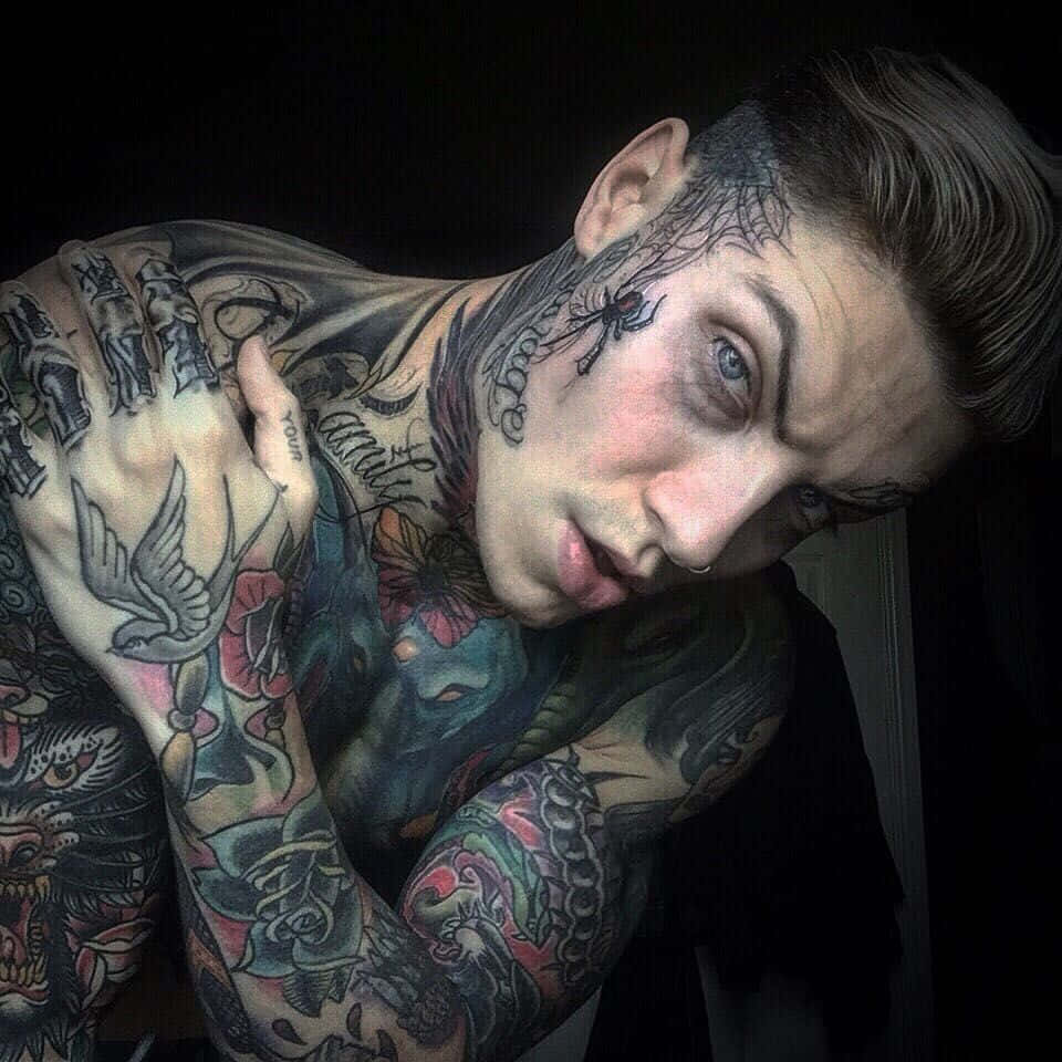 Tattoo Boy 桌布 壁紙 — 一個紋身濃密的男人，擁有引人注目的藍色眼睛，在黑暗背景下凝視著。