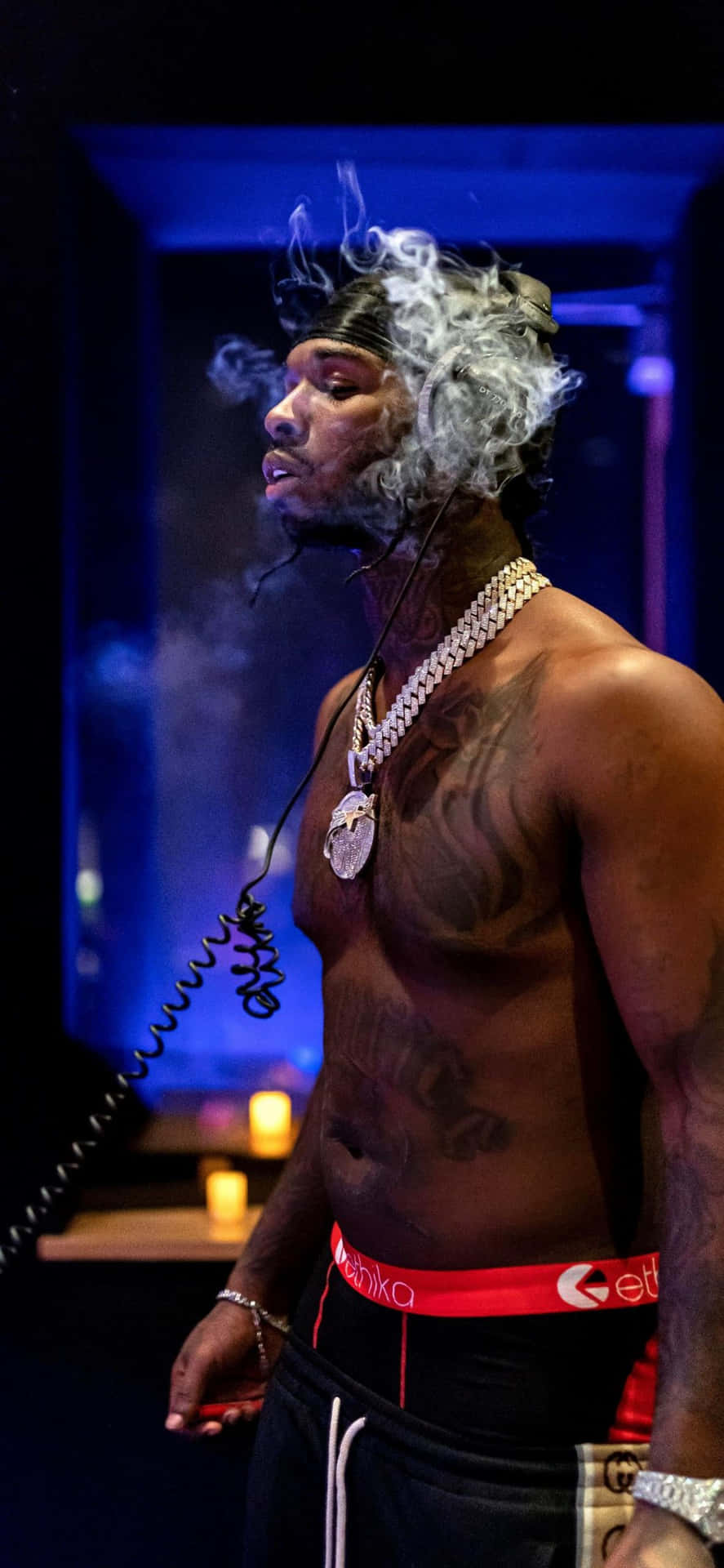 一個紋身男人在黑暗的藍色燈光房間裡與蠟燭一起呼出煙霧。 — Pop Smoke GIF 壁紙
