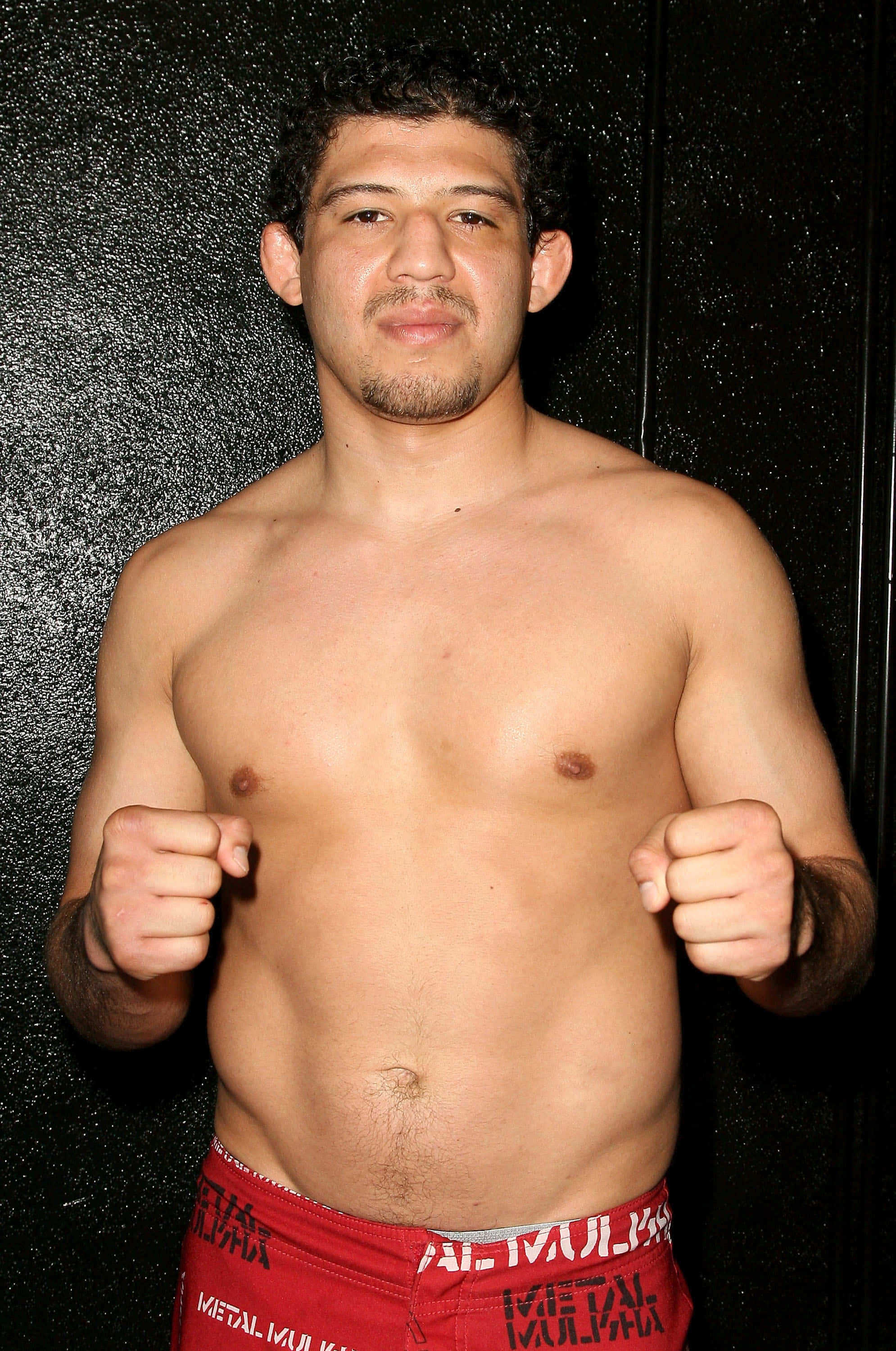 MMA 桌布 壁紙 — 一個紋身肌肉男赤裸上身，穿著紅色內褲，以戰鬥姿勢靠著深色紋理牆壁。