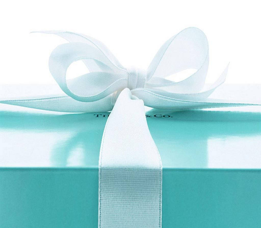 tiffany 桌布 壁紙 — 一個純淨的Tiffany & Co.禮物盒，採用標誌性的知更鳥蛋藍色，頂部繫著完美無瑕的白色緞帶蝴蝶結，背景為明亮的白色。