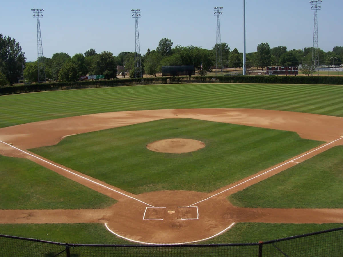 Baseball Field 桌布 壁紙 — 一個純淨的棒球場，擁有鮮綠的草地和棕色的內野，在清澈的藍天下。