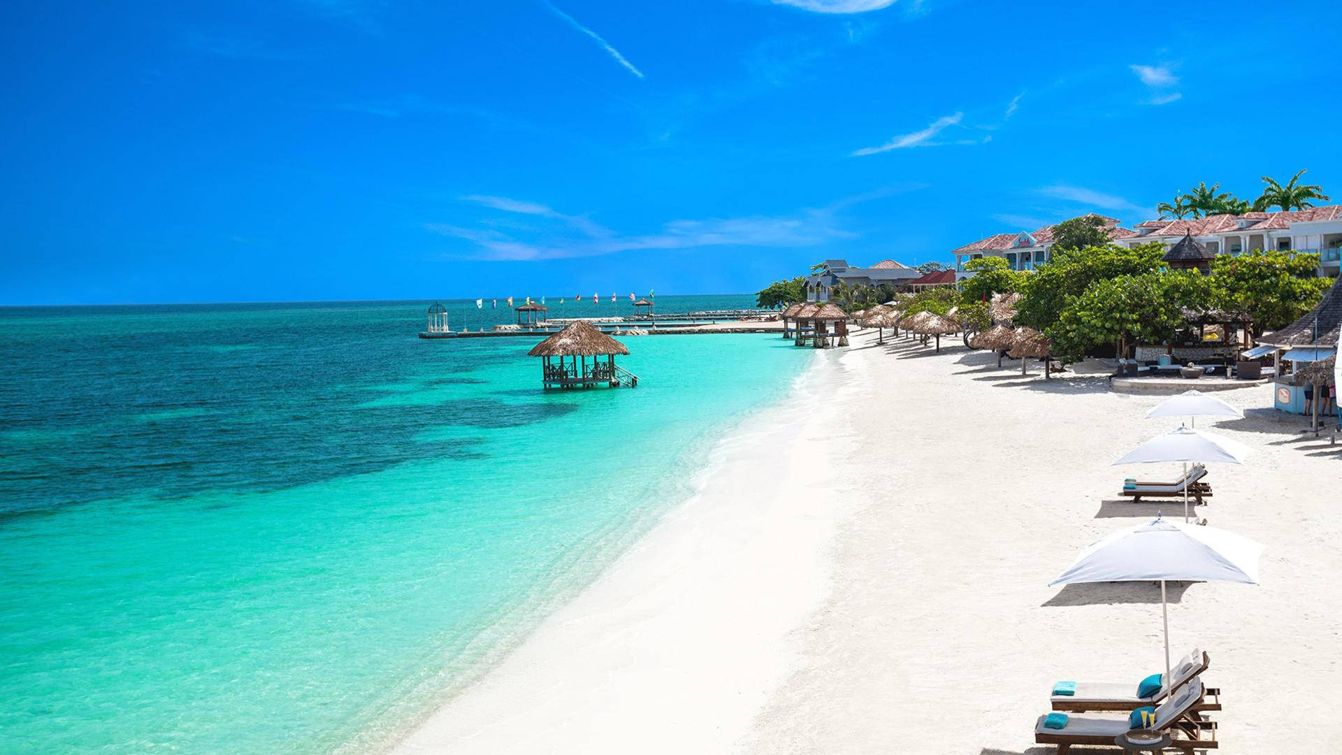 Jamaica 桌布 壁紙 — 一個純淨的熱帶海灘，有碧綠的海水、白色的沙灘和茅草傘，在明亮的藍天下。
