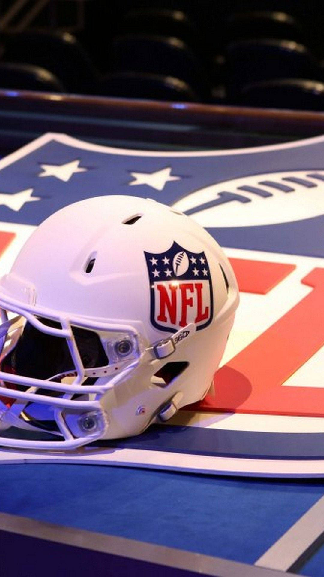 NFL 桌布 壁紙 — 一個純白色的NFL美式足球頭盔放在色彩繽紛的球隊標誌地板上，背景是模糊的體育館座位。
