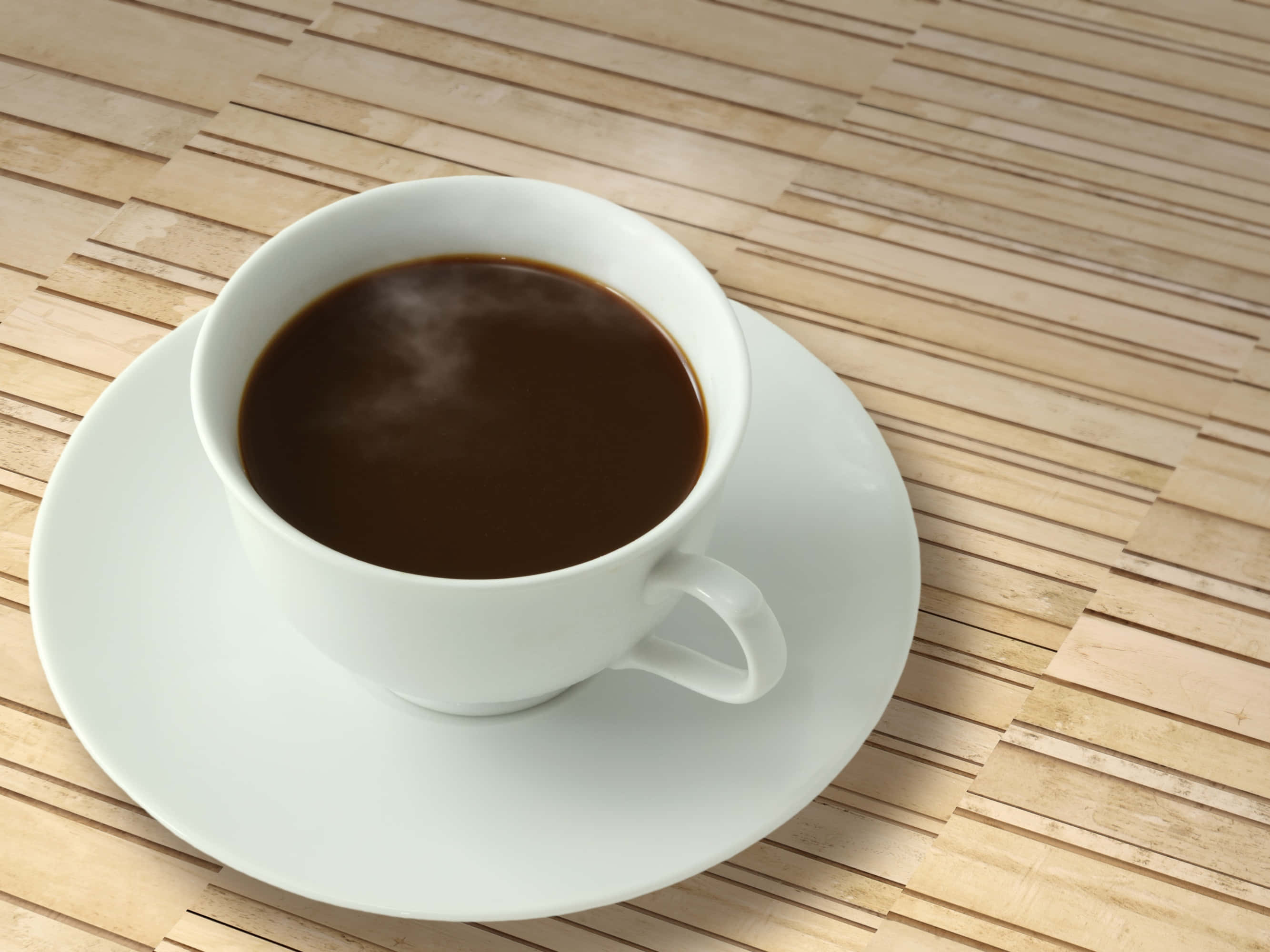 Coffee Cup 桌布 壁紙 — 一個純白色的咖啡杯盛載著深色咖啡，放在淺色木竹蓆上的配套碟子上。