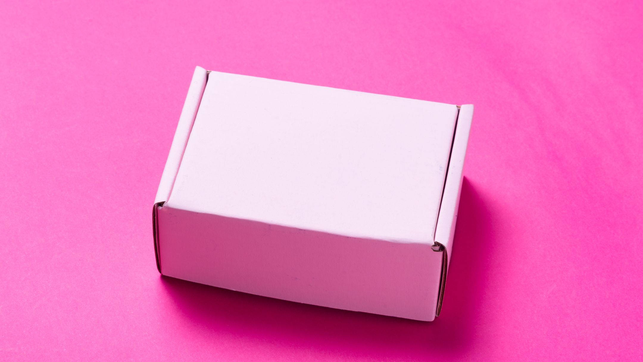 Box 桌布 壁紙 — 一個純白色紙箱在柔和工作室燈光下，居中放置在鮮豔粉紅色紋理表面上。