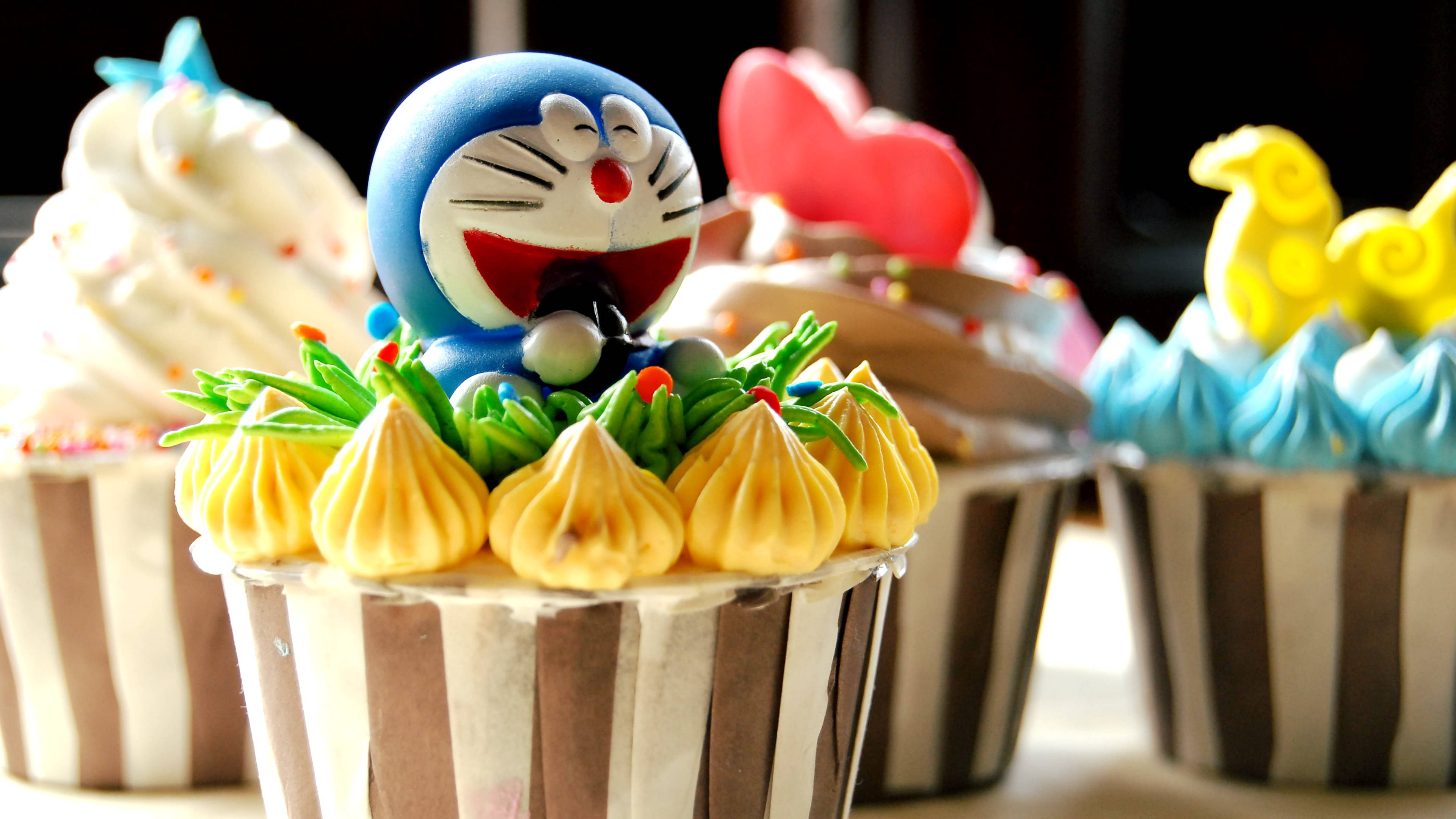 Doraemon 桌布 壁紙 — 一個紙杯蛋糕的特寫，上面放著一個微笑的藍色哆啦A夢公仔，周圍環繞著擠花黃色糖霜。