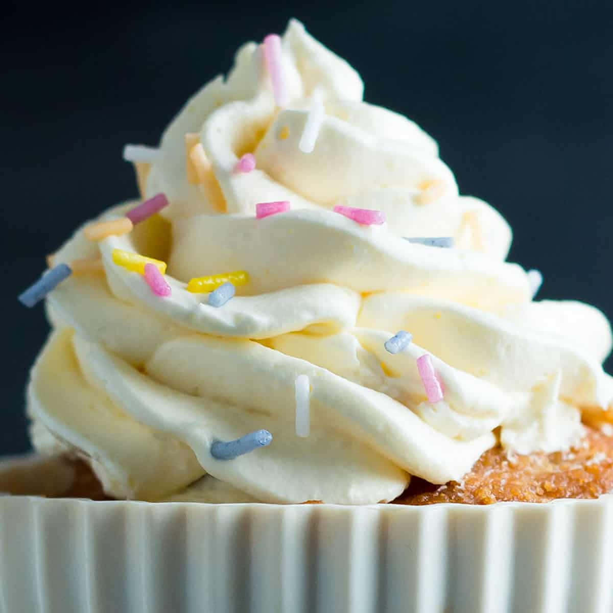 Buttercream 桌布 壁紙 — 一個紙杯蛋糕的特寫，上面有奶油白色糖霜和彩色糖粒，背景為深色。