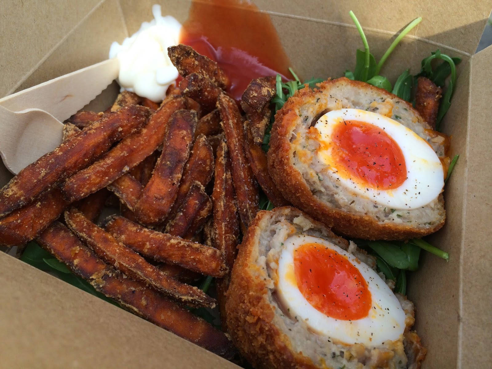 Egg 桌布 壁紙 — 一個紙箱的特寫，裡面裝滿了金黃色的地瓜條和兩個切半的蘇格蘭蛋，蛋黃流出，配上新鮮蔬菜。