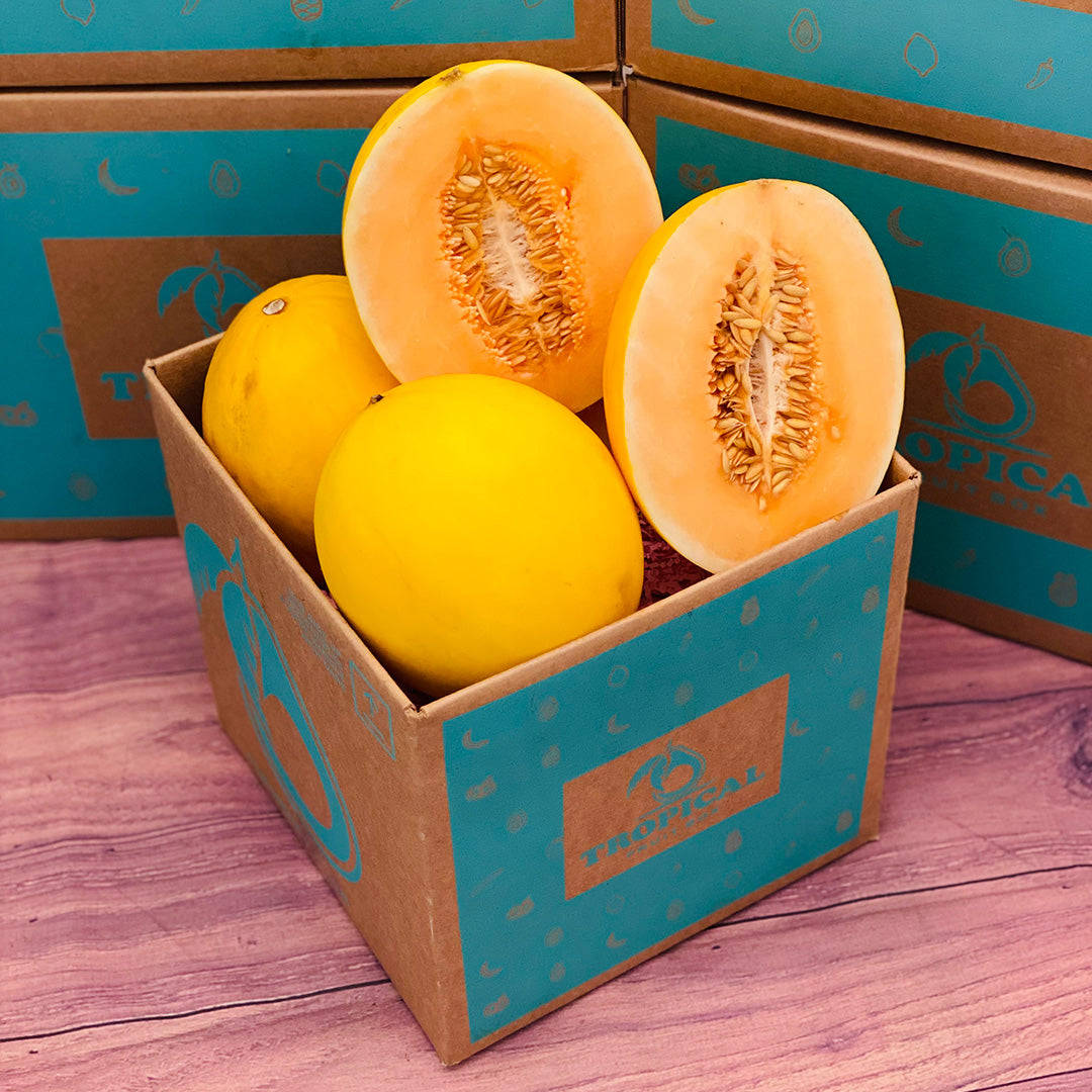 Fruit 桌布 壁紙 — 一個紙箱裝滿了鮮黃色的哈密瓜，有些切開露出橙色果肉和種子，放在粉紅色的木質表面上。