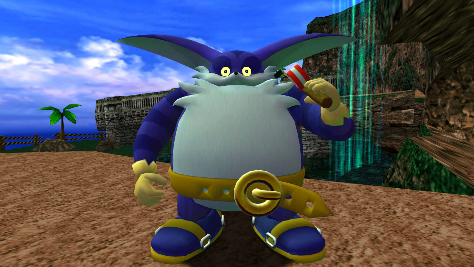Big The Cat 桌布 壁紙 — 一個紫色兔子角色，有白色鬍鬚和黃色腰帶，站在沙灘上，附近有瀑布和棕櫚樹。