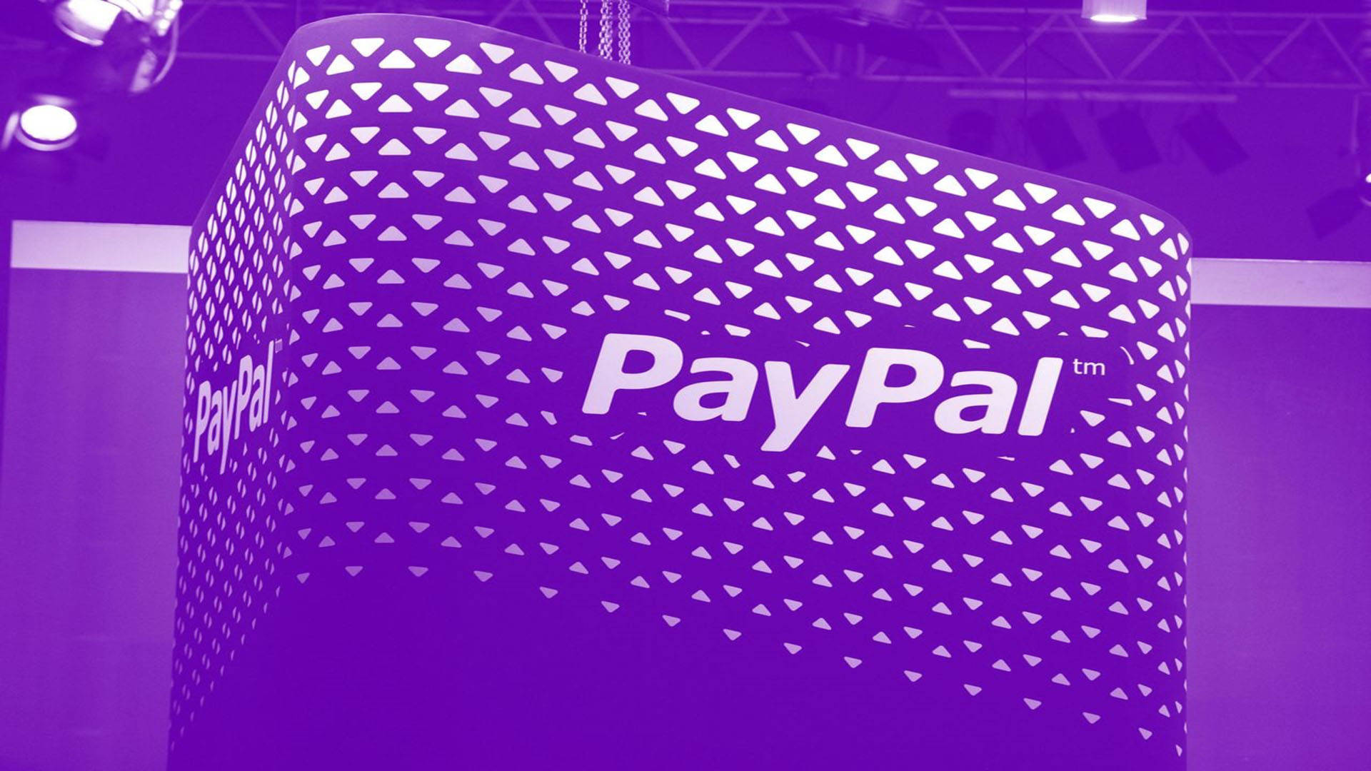 PayPal 桌布 壁紙 — 一個紫色幾何圖案的PayPal攤位在展覽會上亮起，可見頭頂燈光和桁架結構。