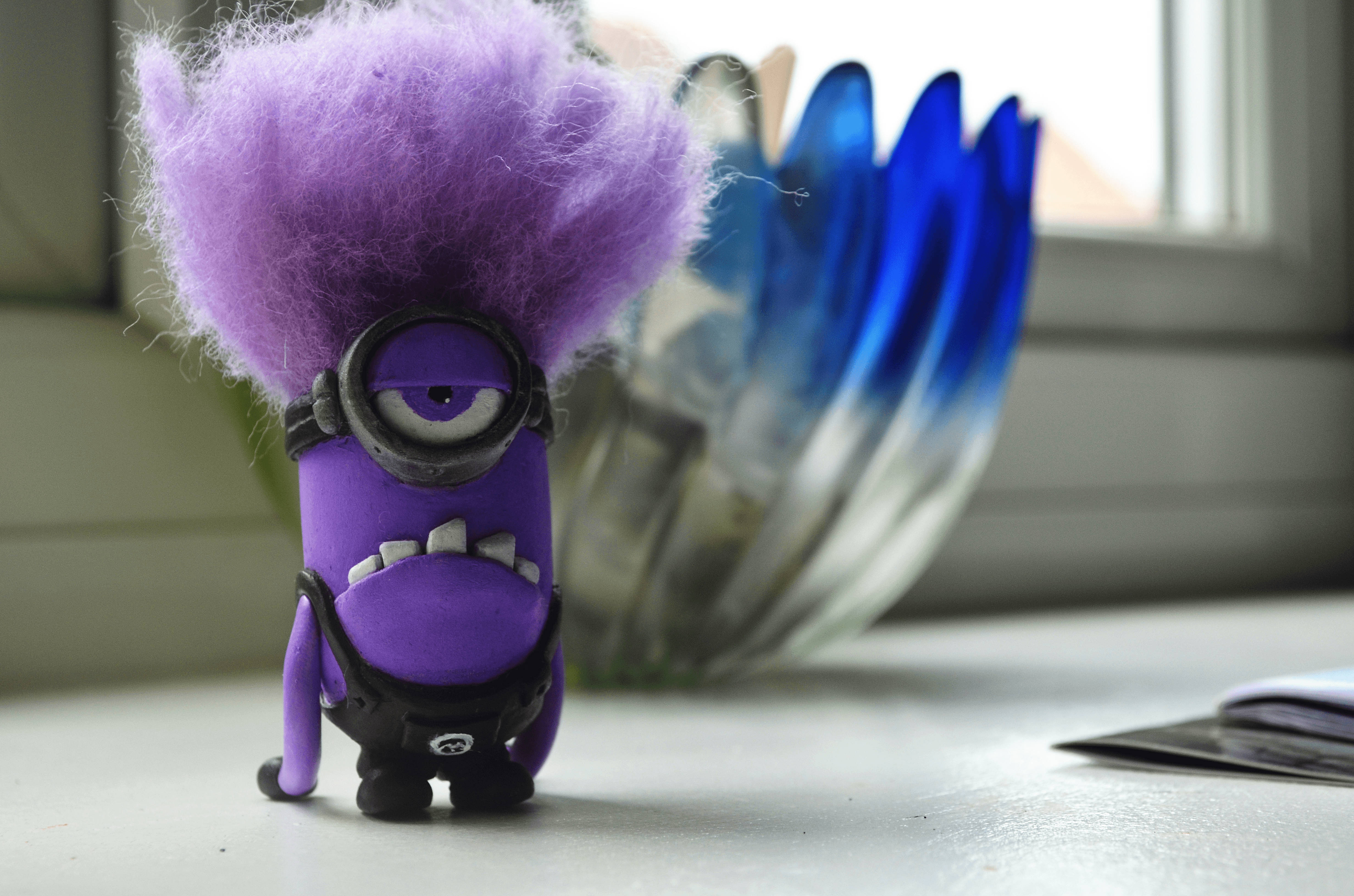 Evil Minion 桌布 壁紙 — 一個紫色的Minion，有著亂糟糟的頭髮和一隻眼睛，站在窗台上，旁邊有一個藍色玻璃花瓶。