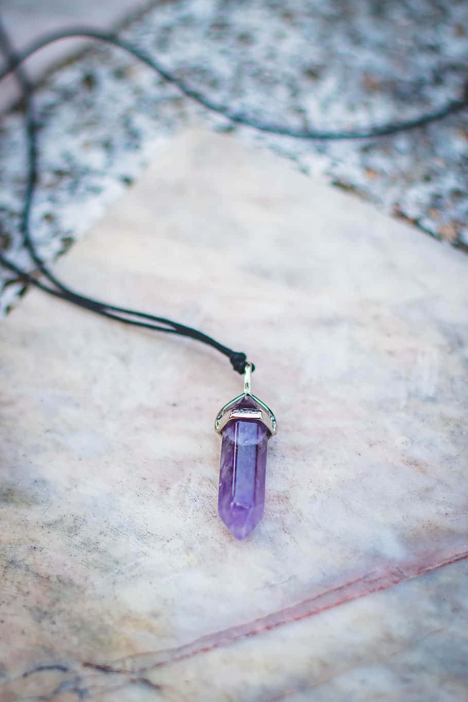 Purple Accessories 桌布 壁紙 — 一個紫色紫水晶水晶吊墜，用銀線包裹，放在淺色帶紋理的大理石表面上。