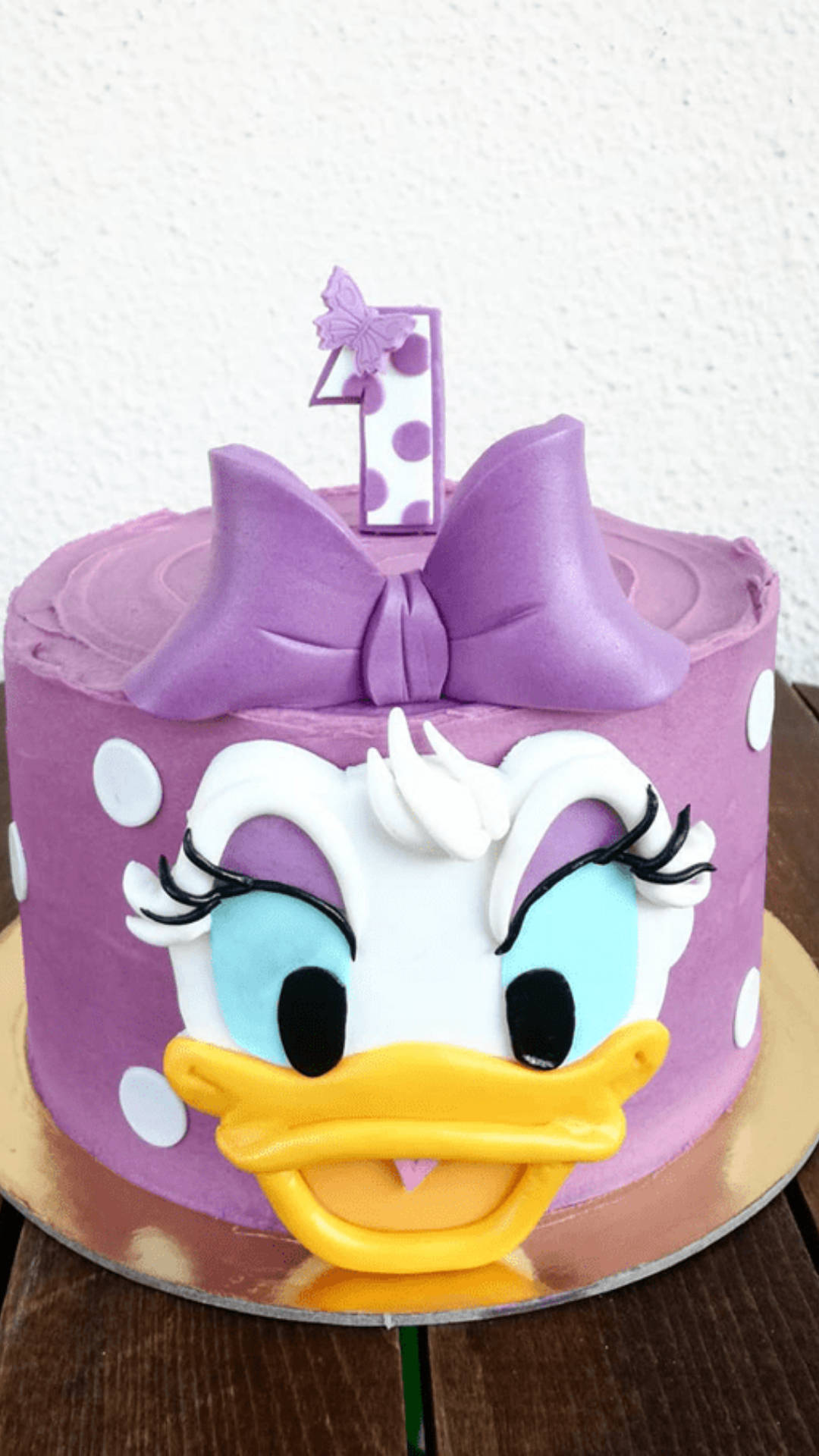 Daisy Duck 桌布 壁紙 — 一個紫色翻糖蛋糕，造型像黛絲鴨，有白色圓點和一個大蝴蝶結，頂上插著一支數字一蠟燭。