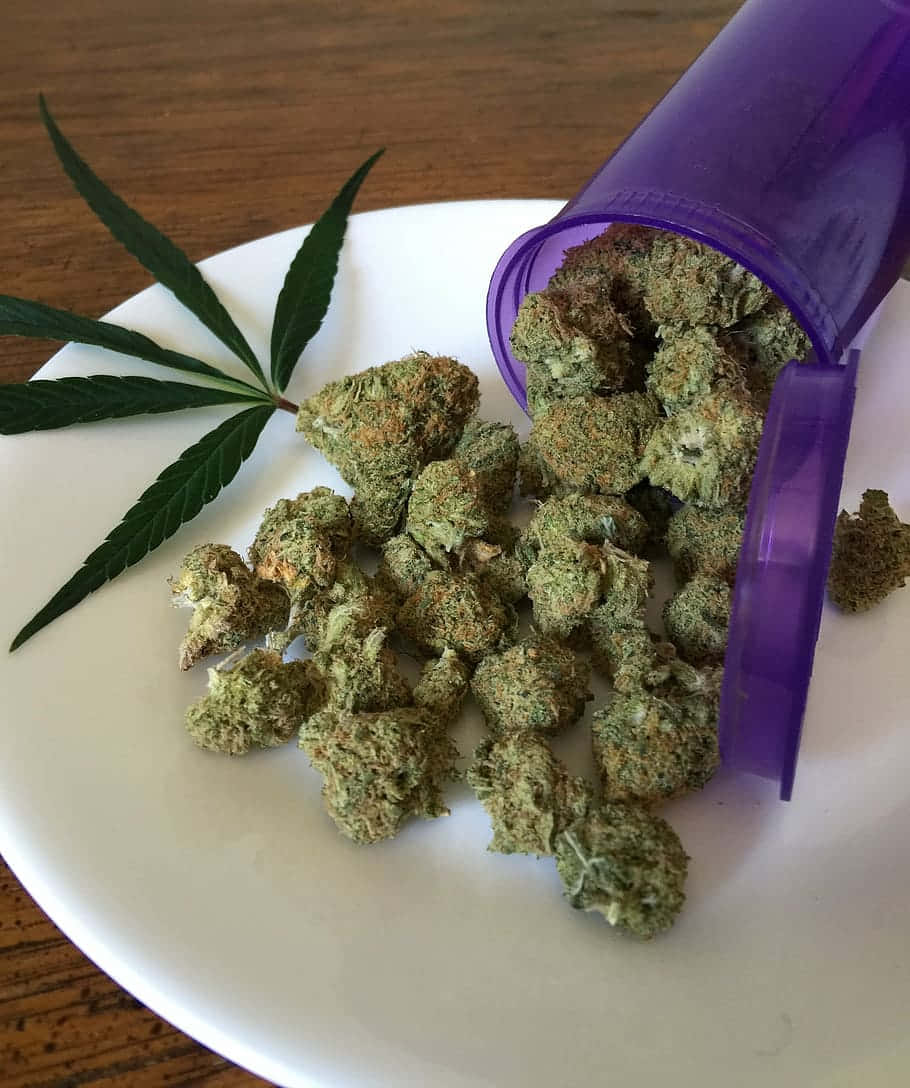  壁紙 — 一個紫色藥瓶翻倒，將綠色大麻花蕾灑在白色盤子上，旁邊有一片大麻葉，放在木桌上。