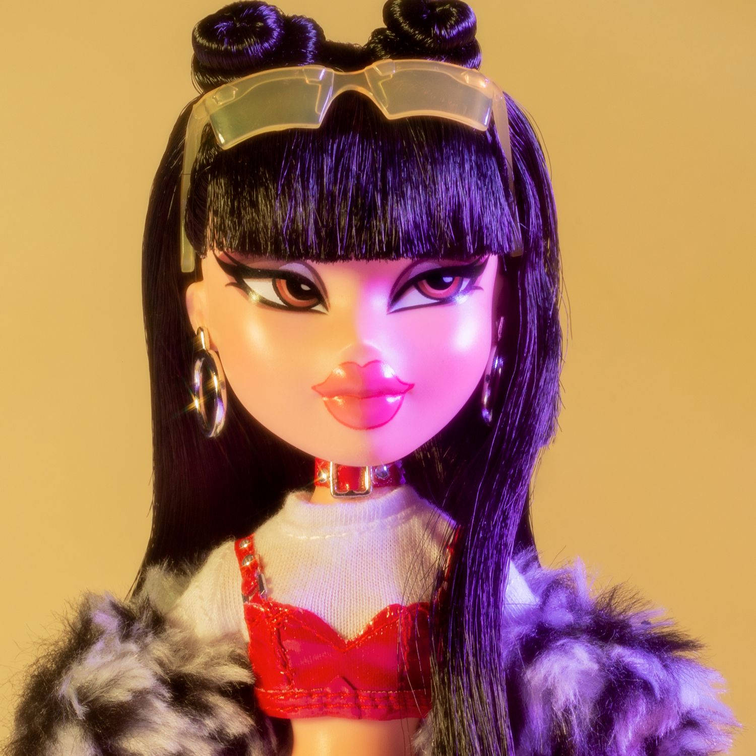Bratz 桌布 壁紙 — 一個紫色頭髮、戴著未來感眼鏡的娃娃，在溫暖的黃色背景前擺姿勢，身穿紅色上衣和毛皮外套。