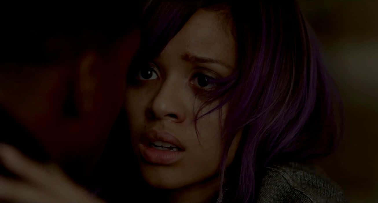 Gugu Mbatha-raw 桌布 壁紙 — 一個紫色頭髮的女人在昏暗的場景中，看著一個陰影人物逼近，顯得驚恐萬分。