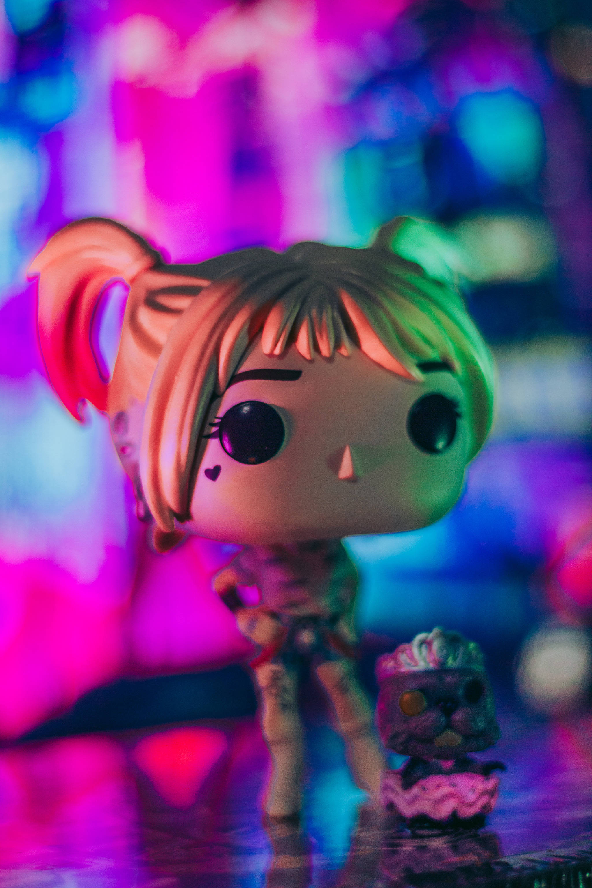 pop 桌布 壁紙 — 一個紮辮子的Funko Pop公仔站在一個小蛋糕旁邊，在充滿活力的粉紅色和藍色霓虹燈下。