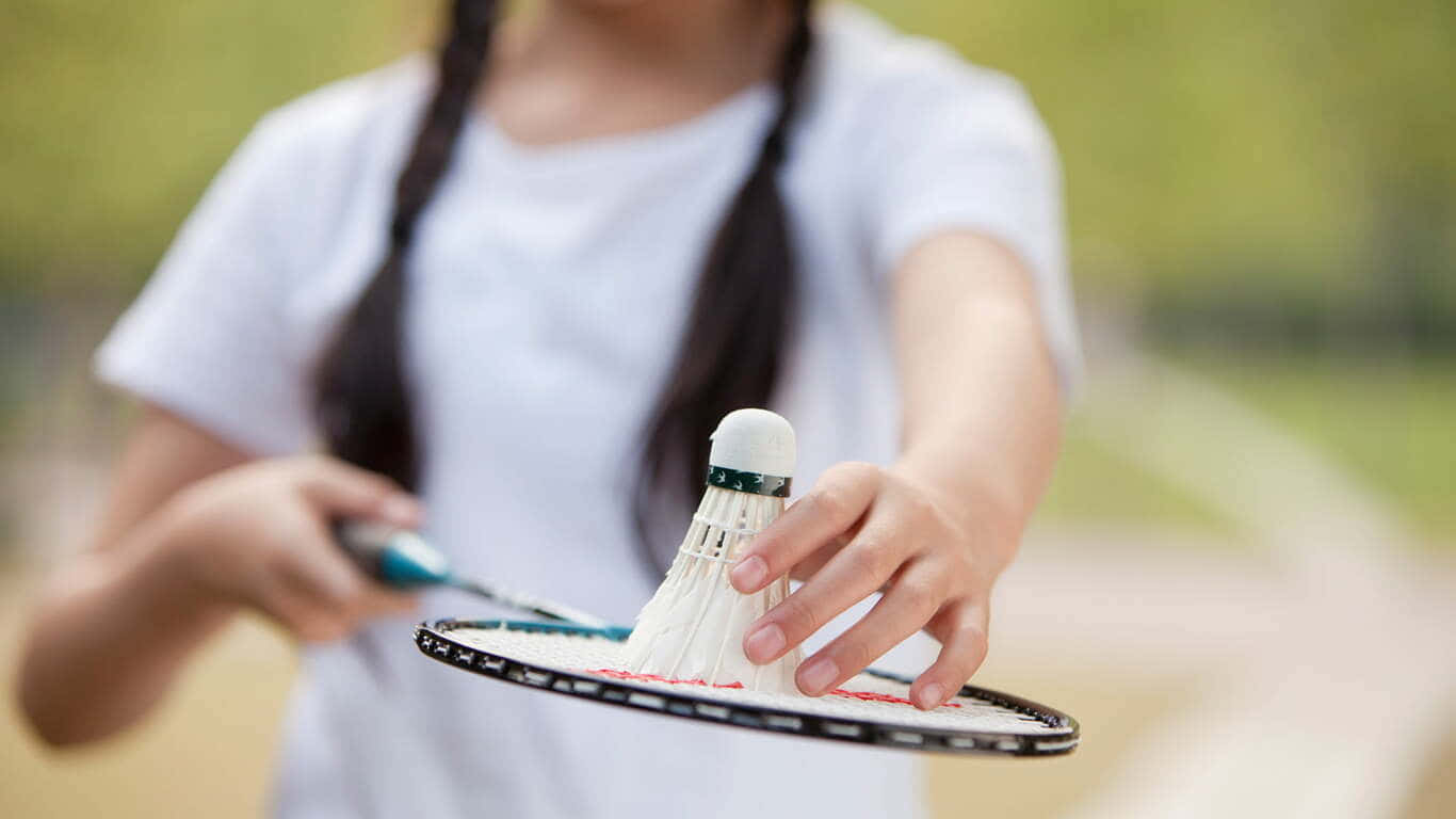 1366x768 Badminton 桌布 壁紙 — 一個紮辮子的年輕女孩在陽光普照的戶外環境中拿著羽毛球拍和羽毛球。