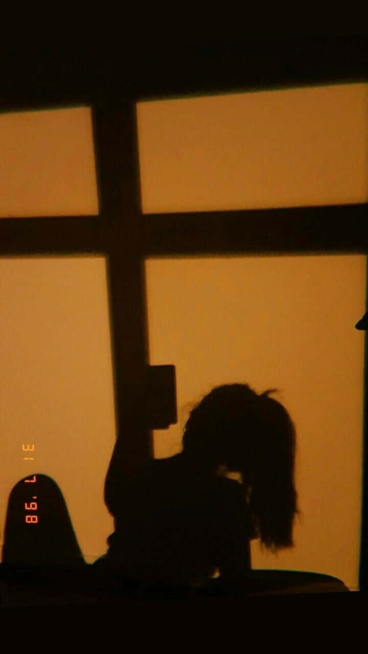 Girl Shadow 桌布 壁紙 — 一個紮馬尾的人的剪影坐在窗邊，溫暖的金色光芒灑滿房間。