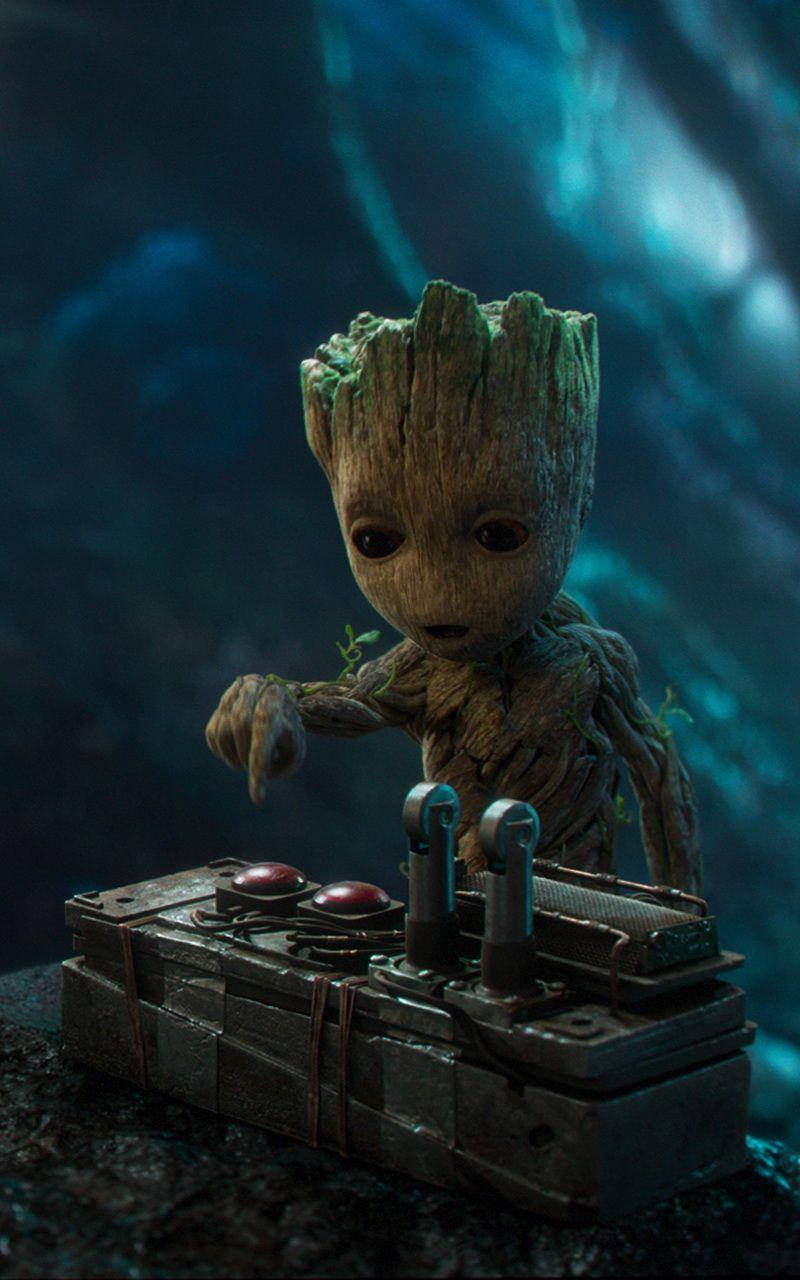 Baby Groot 桌布 壁紙 — 一個細小、像樹木一樣、皮膚長滿苔蘚、眼睛大大的生物，在深藍色的水下場景中，按壓著一個堅固的金屬控制台上的按鈕。