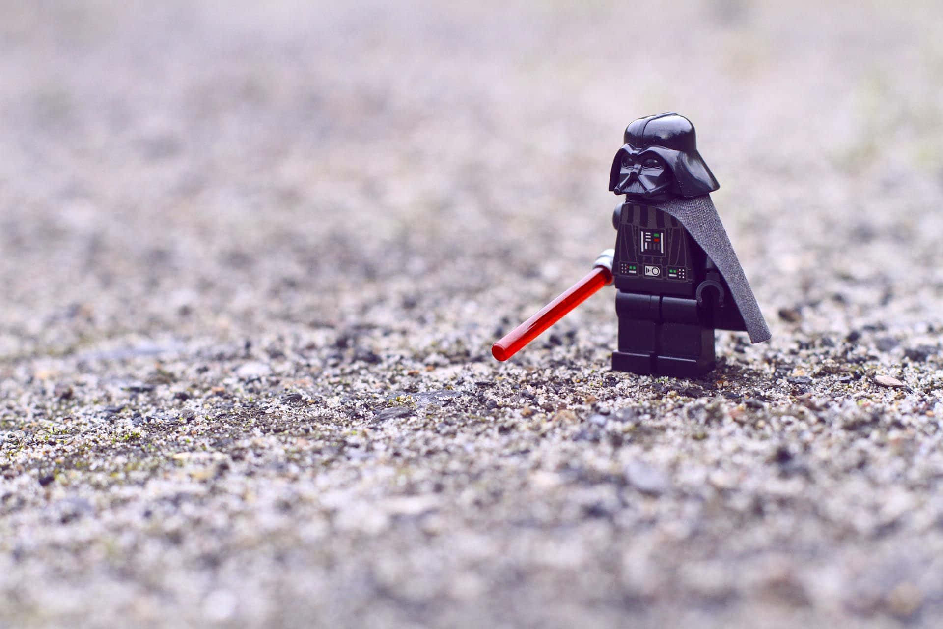 Hipster Desktop 桌布 壁紙 — 一個細小的LEGO黑武士人偶獨自站在粗糙的礫石上，手持紅色光劍。