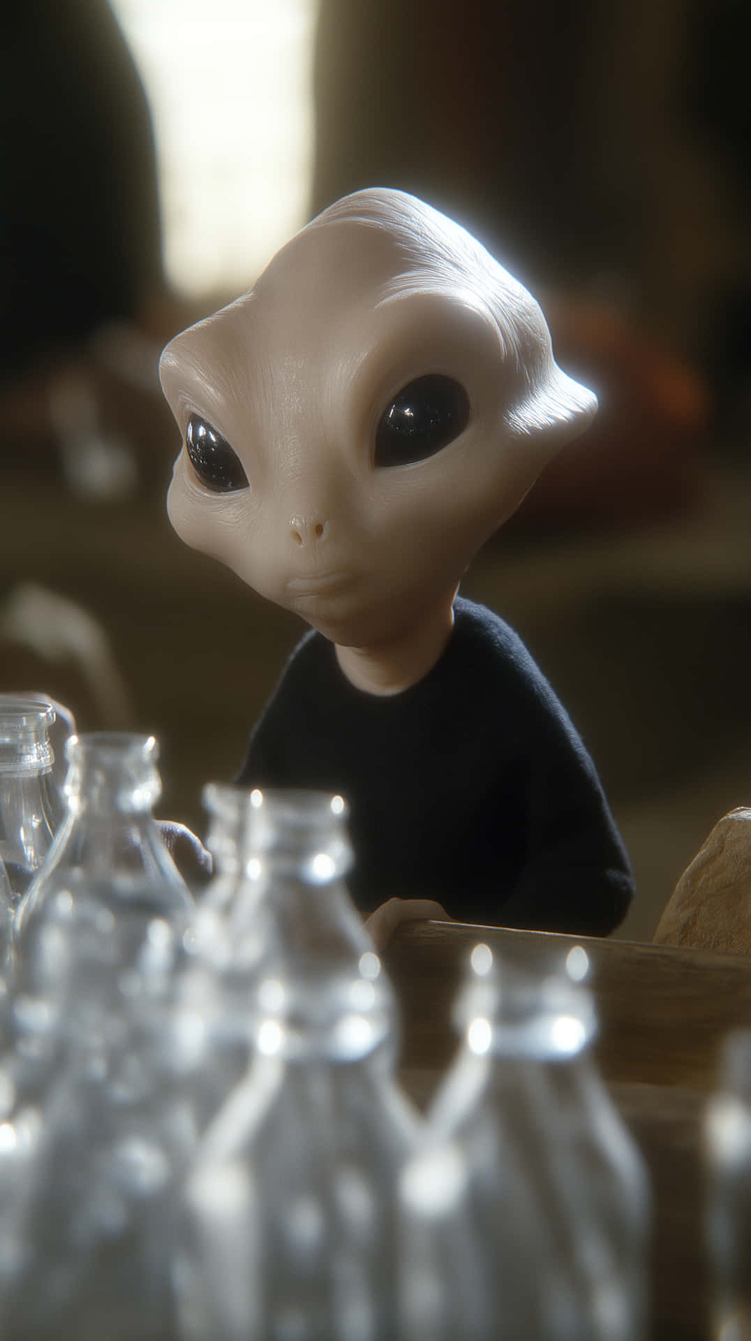 Confused Alien Amidst Empty Bottles - Aftermath Scene 壁紙 — 一個細小的米色外星人，擁有大大的黑色眼睛，坐在木桌旁，周圍是透明的玻璃瓶，在柔和溫暖的光線中。