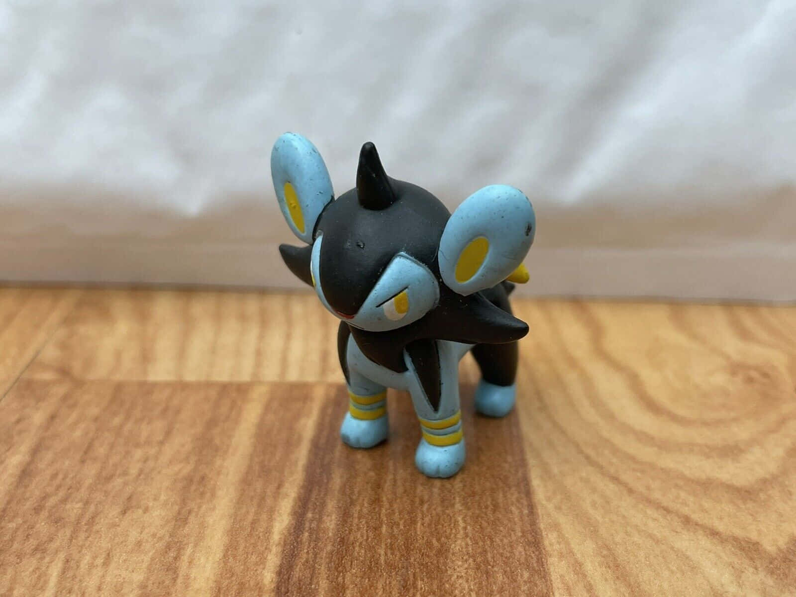 任天堂 桌布 壁紙 — 一個細小的黑色和藍色 Umbreon 寶可夢公仔在木地板上警覺地站立，背景是柔和的白色。