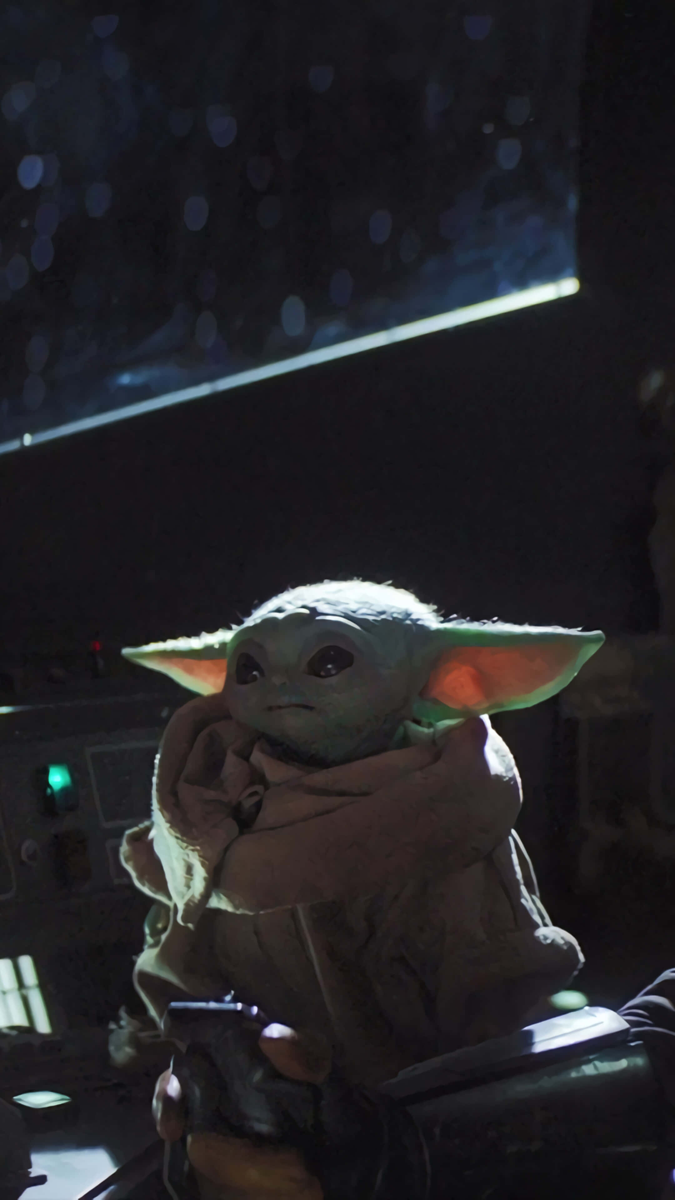 Baby Yoda Phone 桌布 壁紙 — 一個細小綠色大耳外星人坐在昏暗的駕駛艙中，手持爆能槍，在發光面板下若有所思。