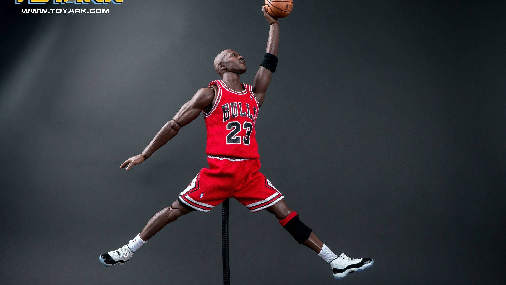 籃球 Jordan 桌布 壁紙 — 一個細節豐富的Michael Jordan動作人偶，身穿標誌性紅色公牛隊球衣，在黑暗工作室背景下空中灌籃。